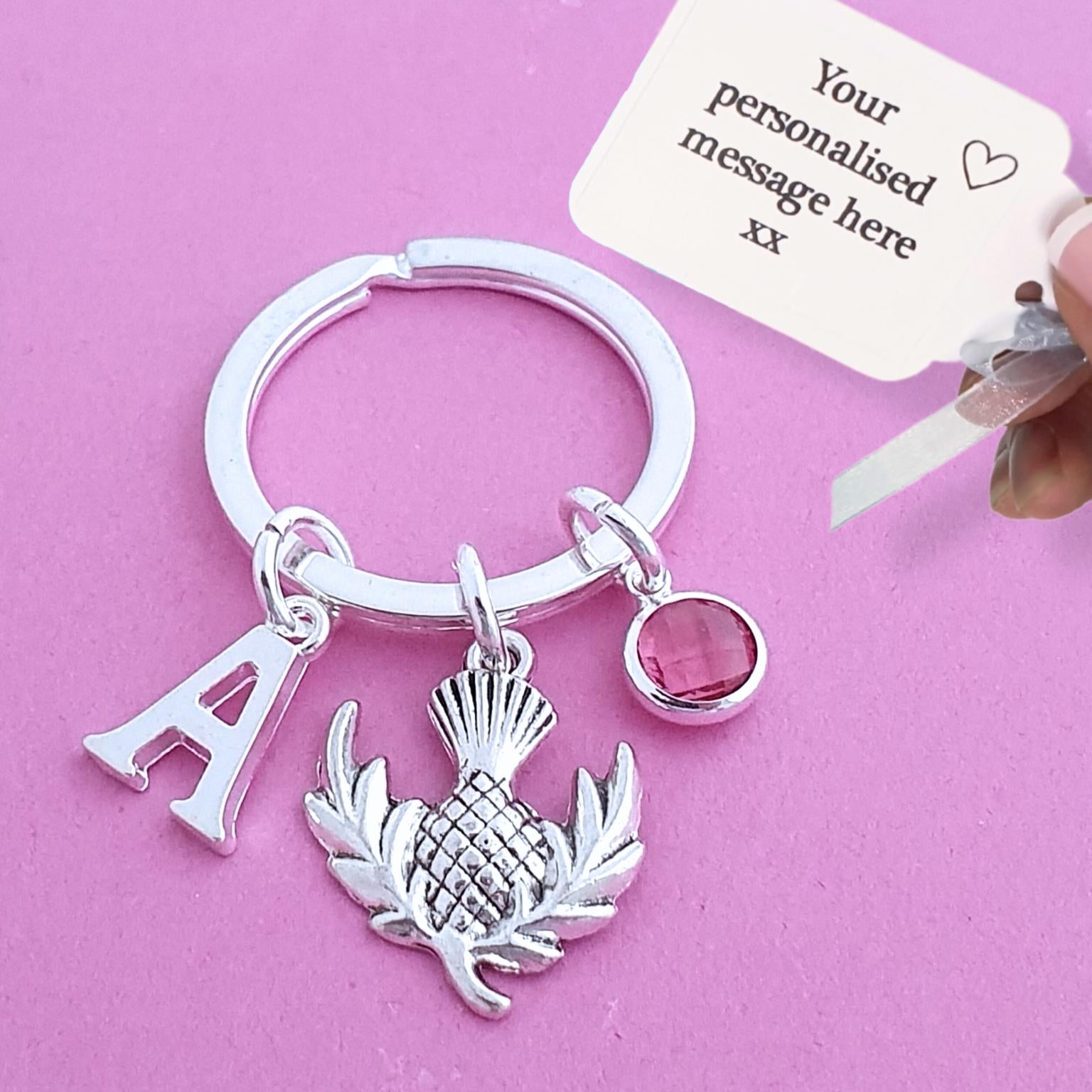 Silver keychain with thistle charm and letter 'A' on a pink background