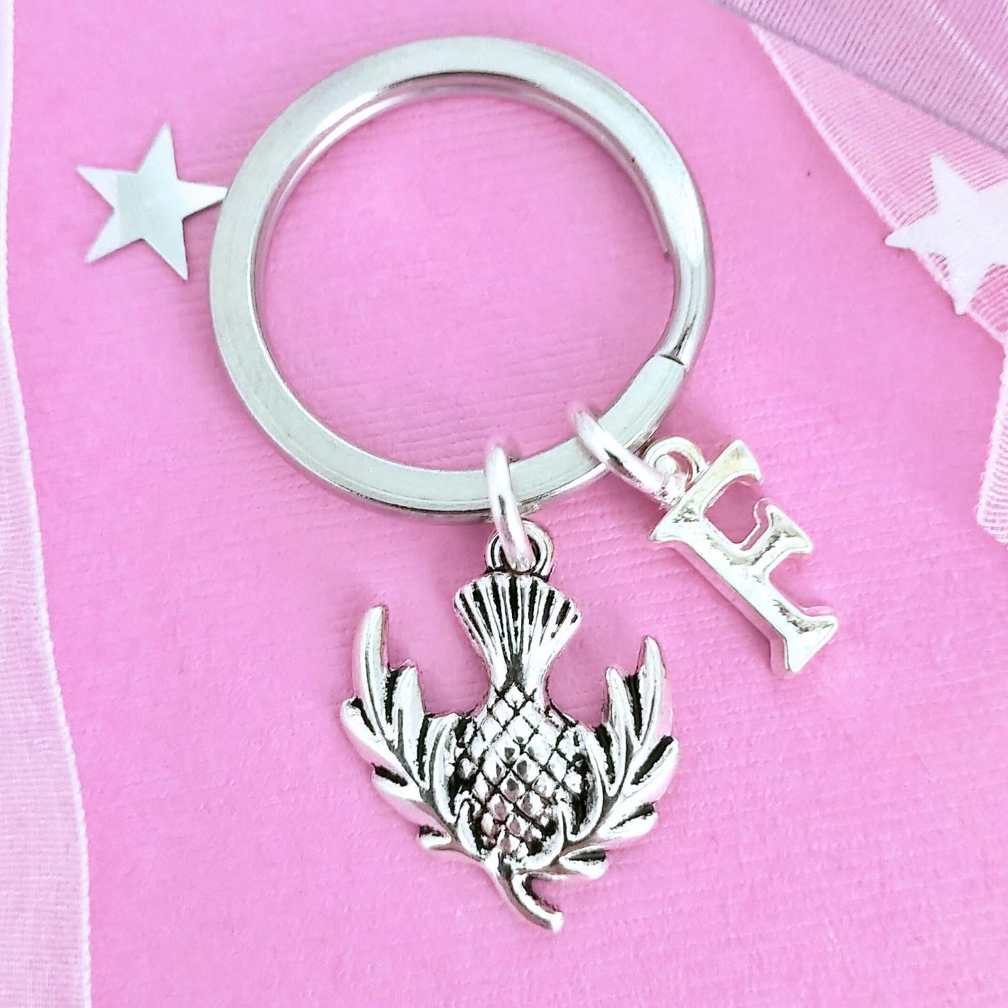 Silver keychain with a thistle charm and letter 'I' on a pink background