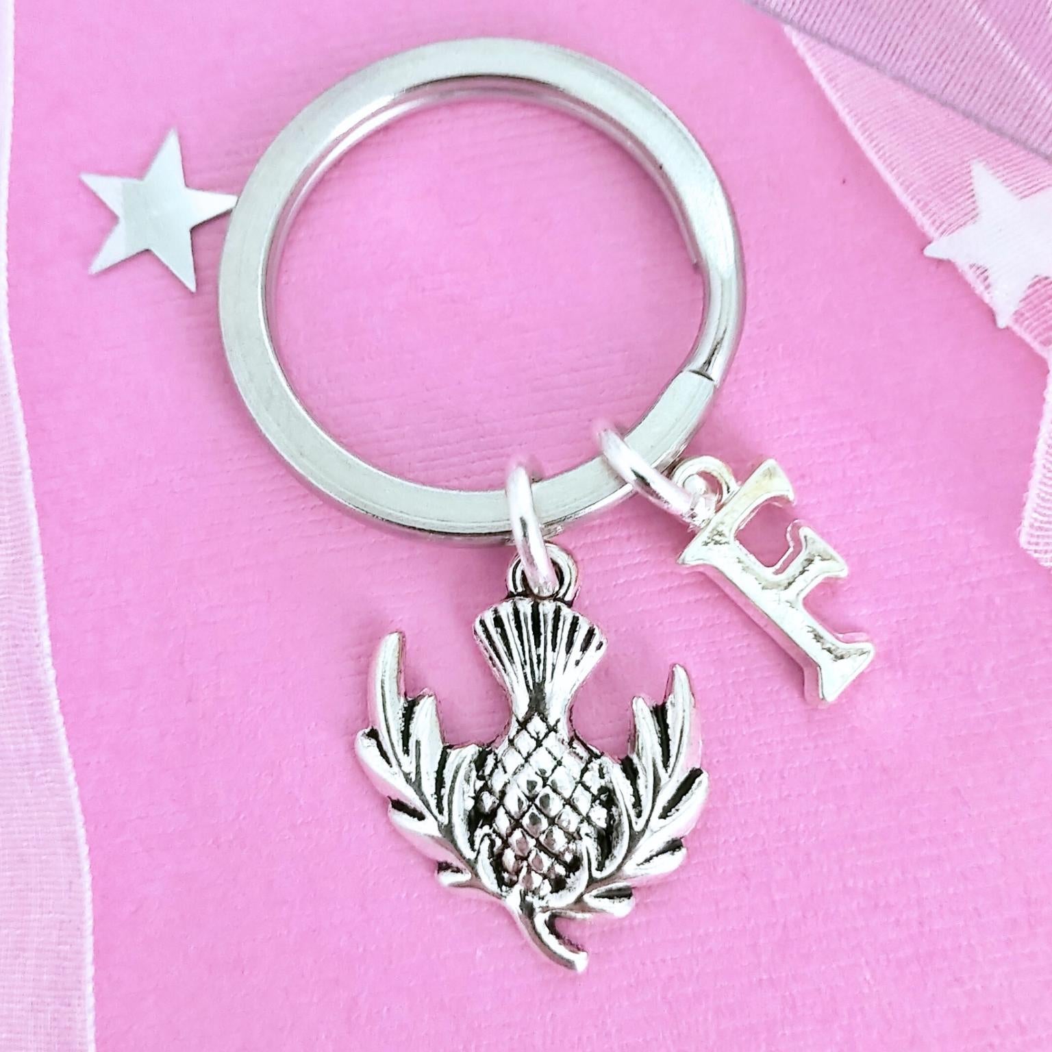 Silver keychain with a thistle charm and letter 'I' on a pink background