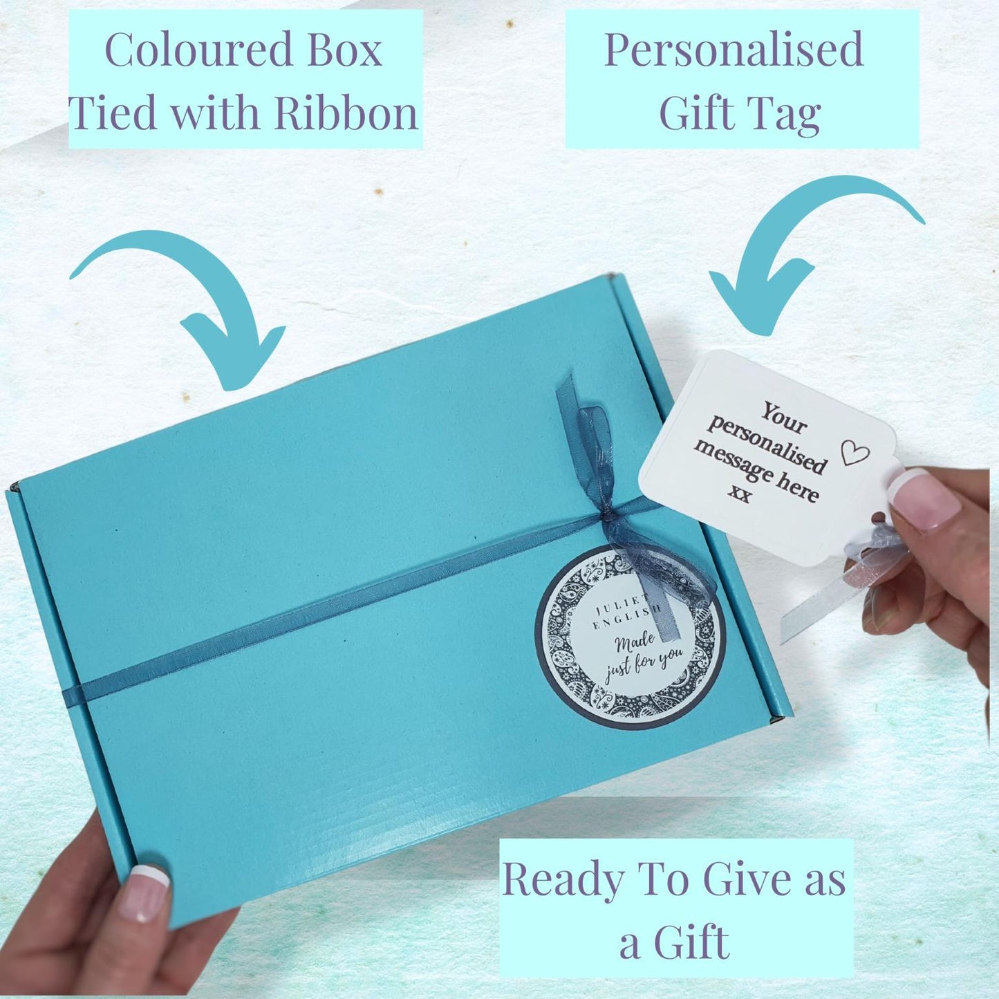 A turquoise gift box tied with a matching ribbon, shown with a hand holding a personalized gift tag. Text overlays highlight the features: 'Coloured Box Tied with Ribbon', 'Personalised Gift Tag', and 'Ready To Give as a Gift'.