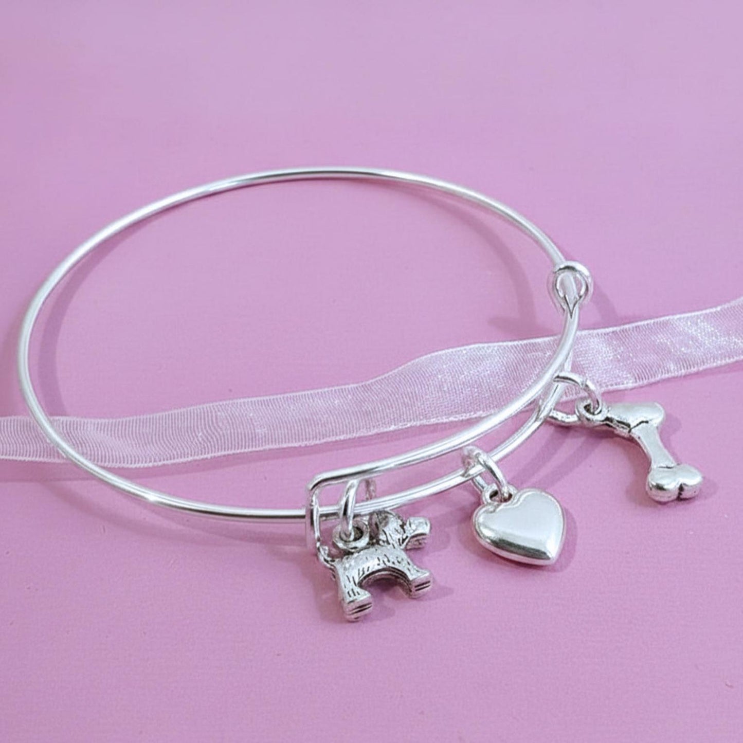 Silver bracelet with various scotty dog theme charms on a pink background
