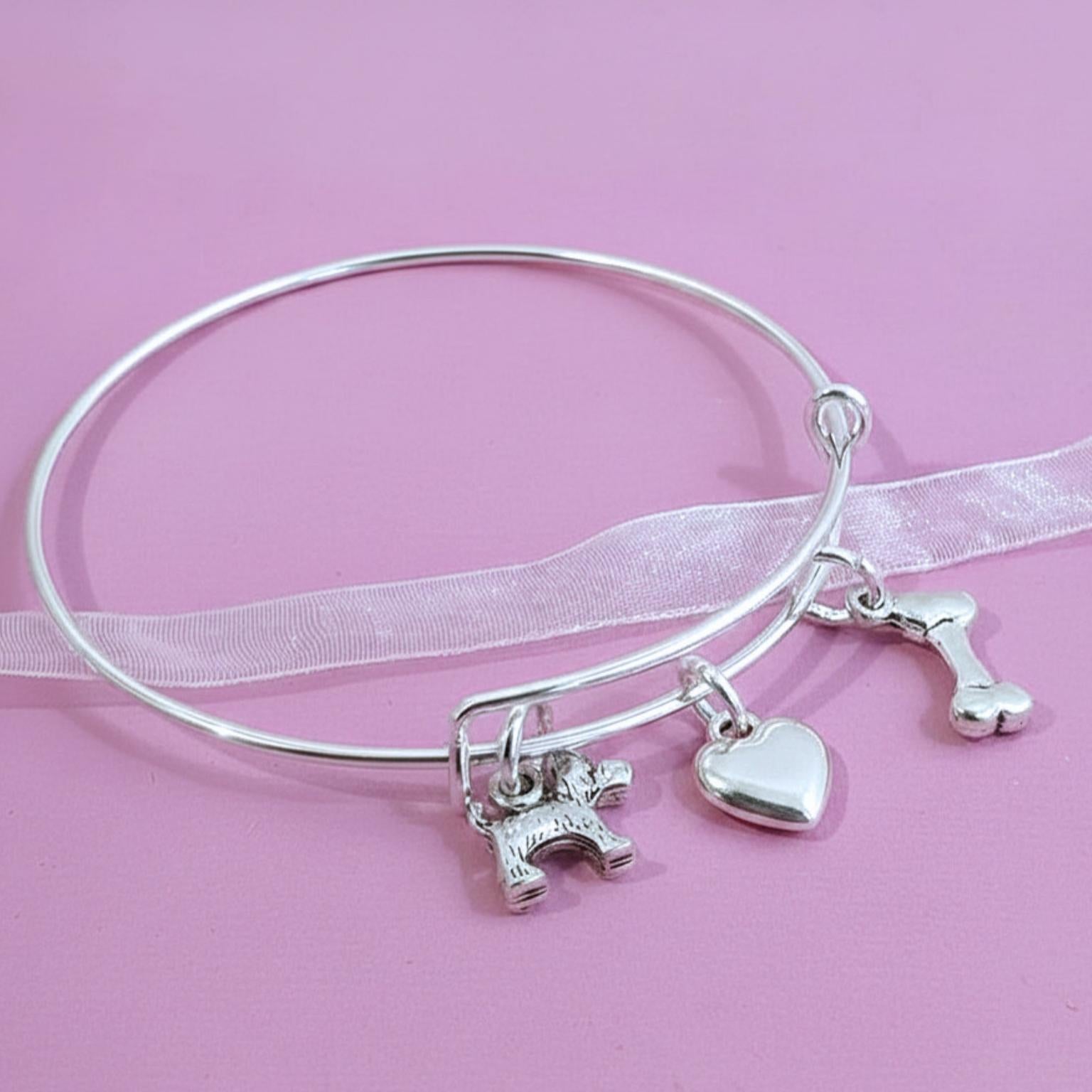 Silver bracelet with various scotty dog theme charms on a pink background