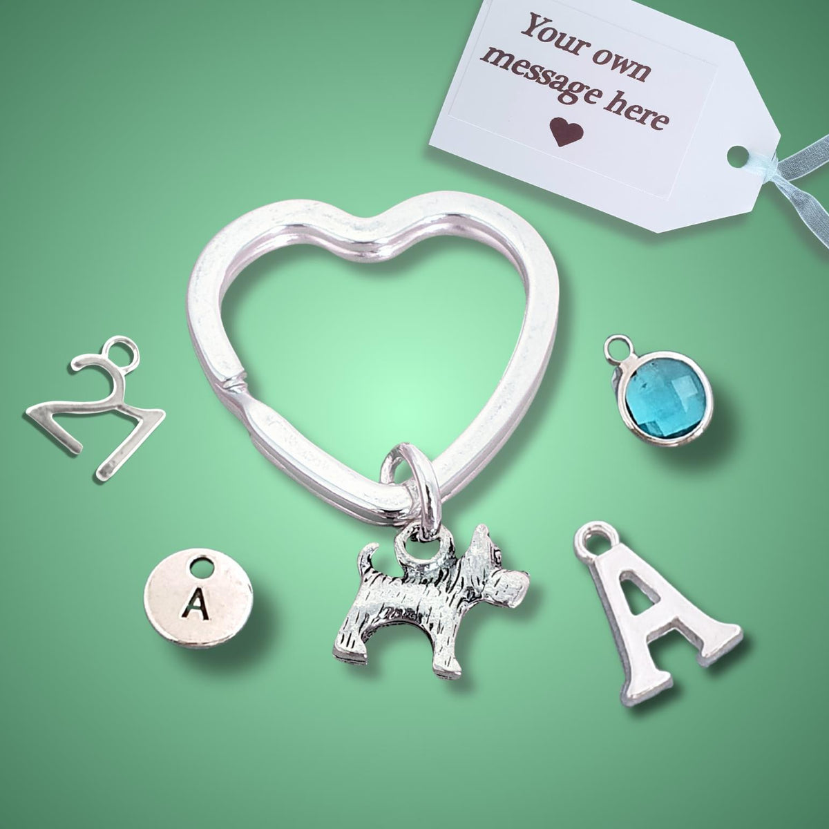 Silver initial charm kit featuring a heart-shaped clasp with a scotty dog charm, an 'A' initial charm, a round initial 'A' disc, a blue gemstone charm, and a person charm, displayed on a green background with a customization tag.