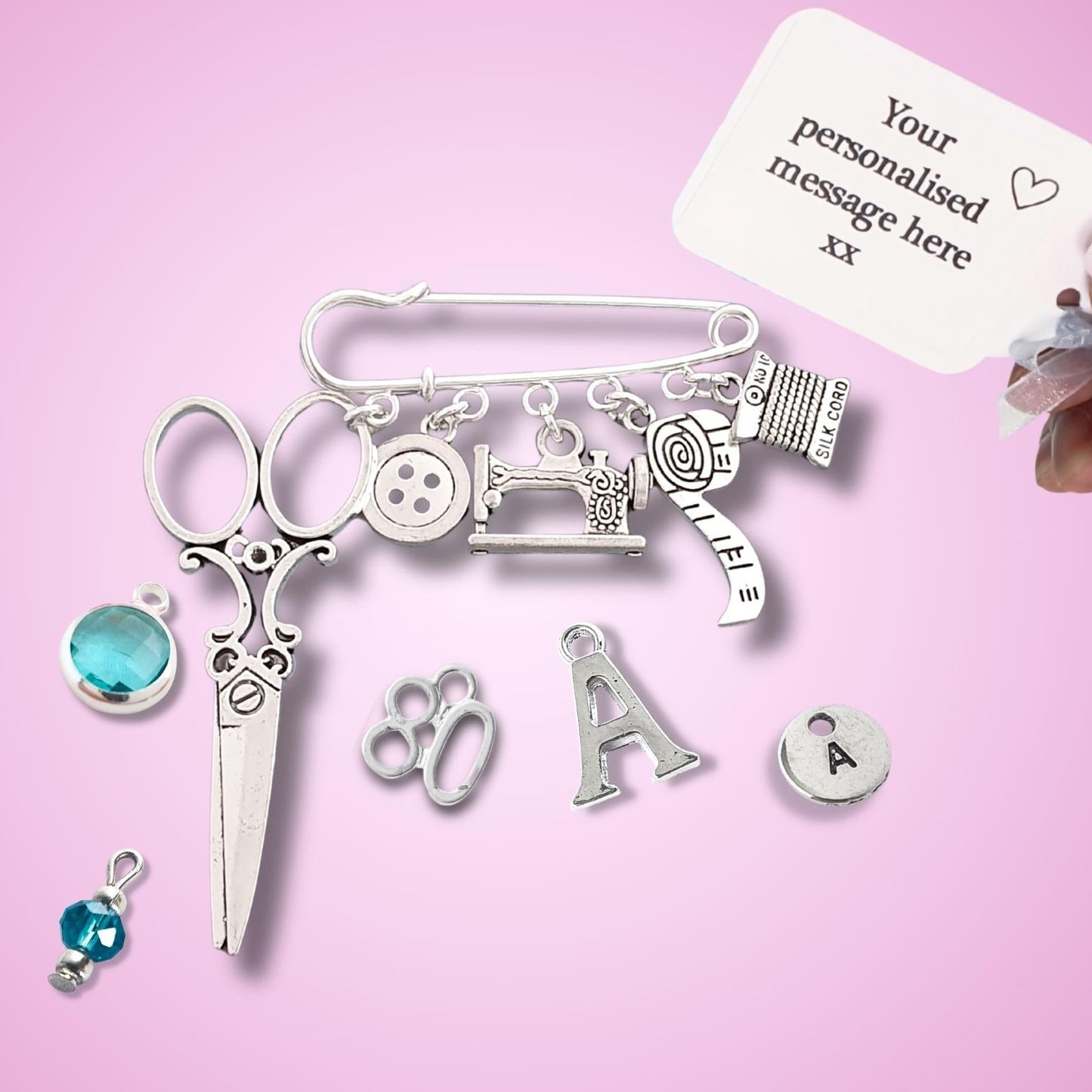 Brooch with sewing themed silver charms including scissors, sewing machine, buttons, on a pink background