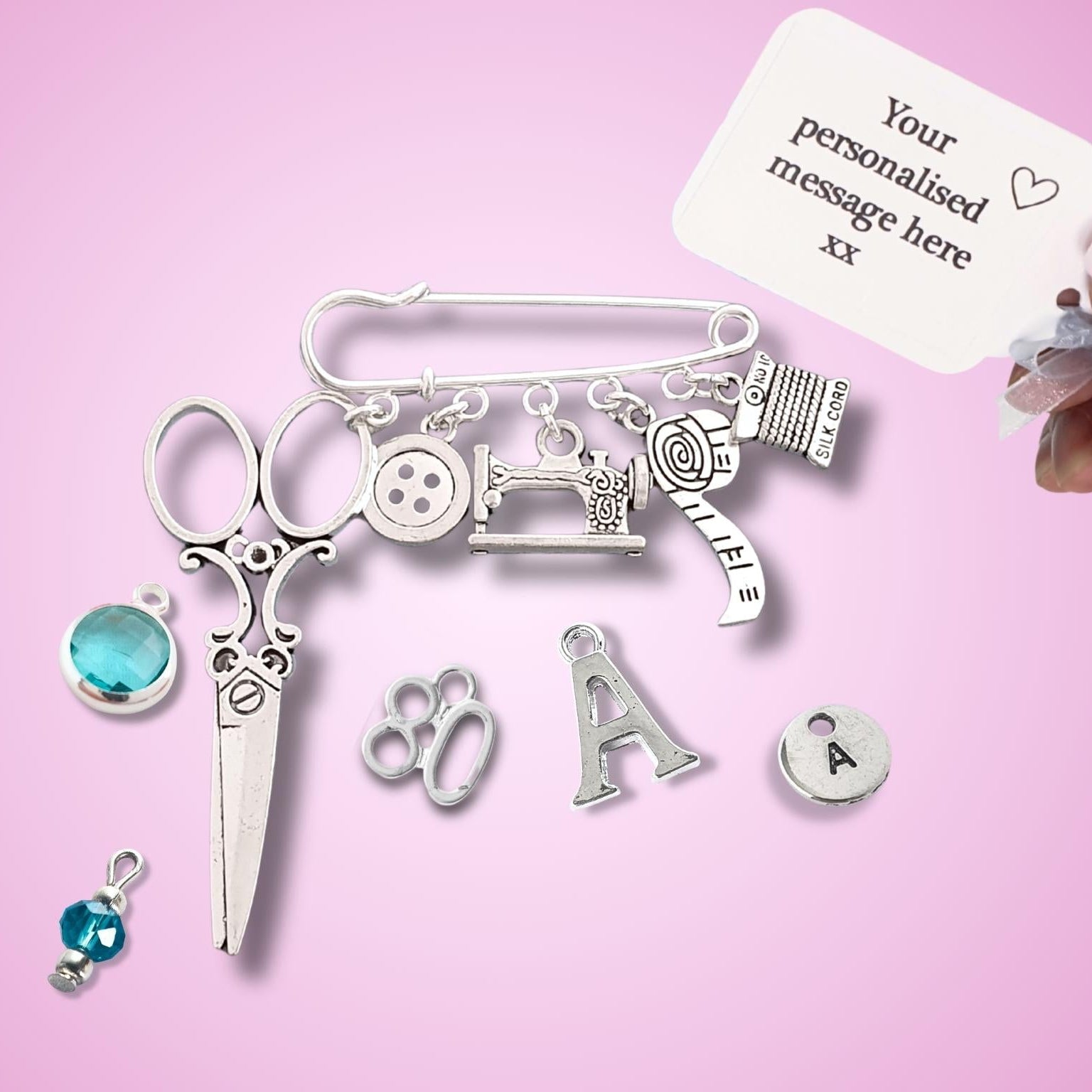 Brooch with sewing themed silver charms including scissors, sewing machine, buttons, on a pink background