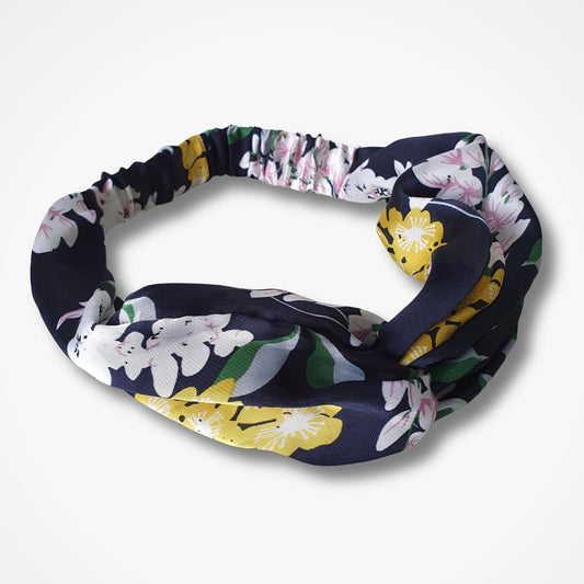 A fabric headband with a dark navy blue background and a colorful floral print featuring white, pink, yellow, and green flowers, shown on a light gray background.
