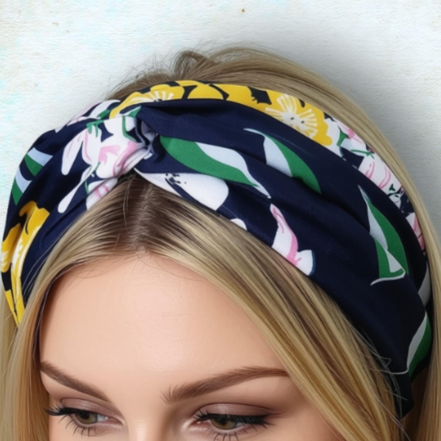 A close-up of a woman wearing a knotted headband with a black, yellow, green, and pink floral pattern against a light blue textured background.