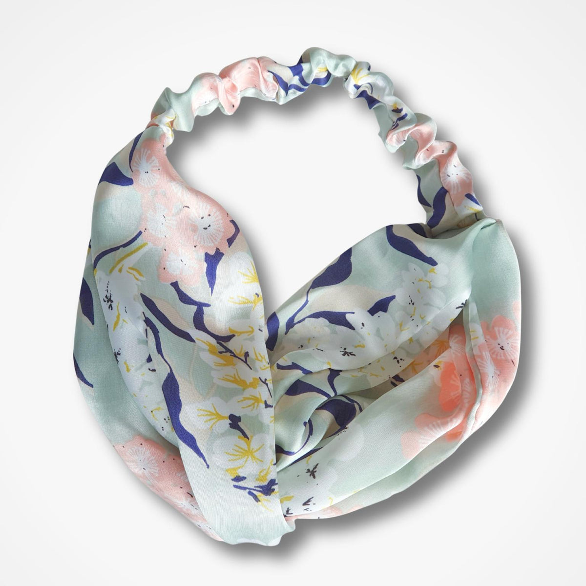 A lightweight, gathered twist knot hairbandwith a watercolor-style print in pastel pink, navy blue, and yellow on a pale mint green background, shown against a plain white background.