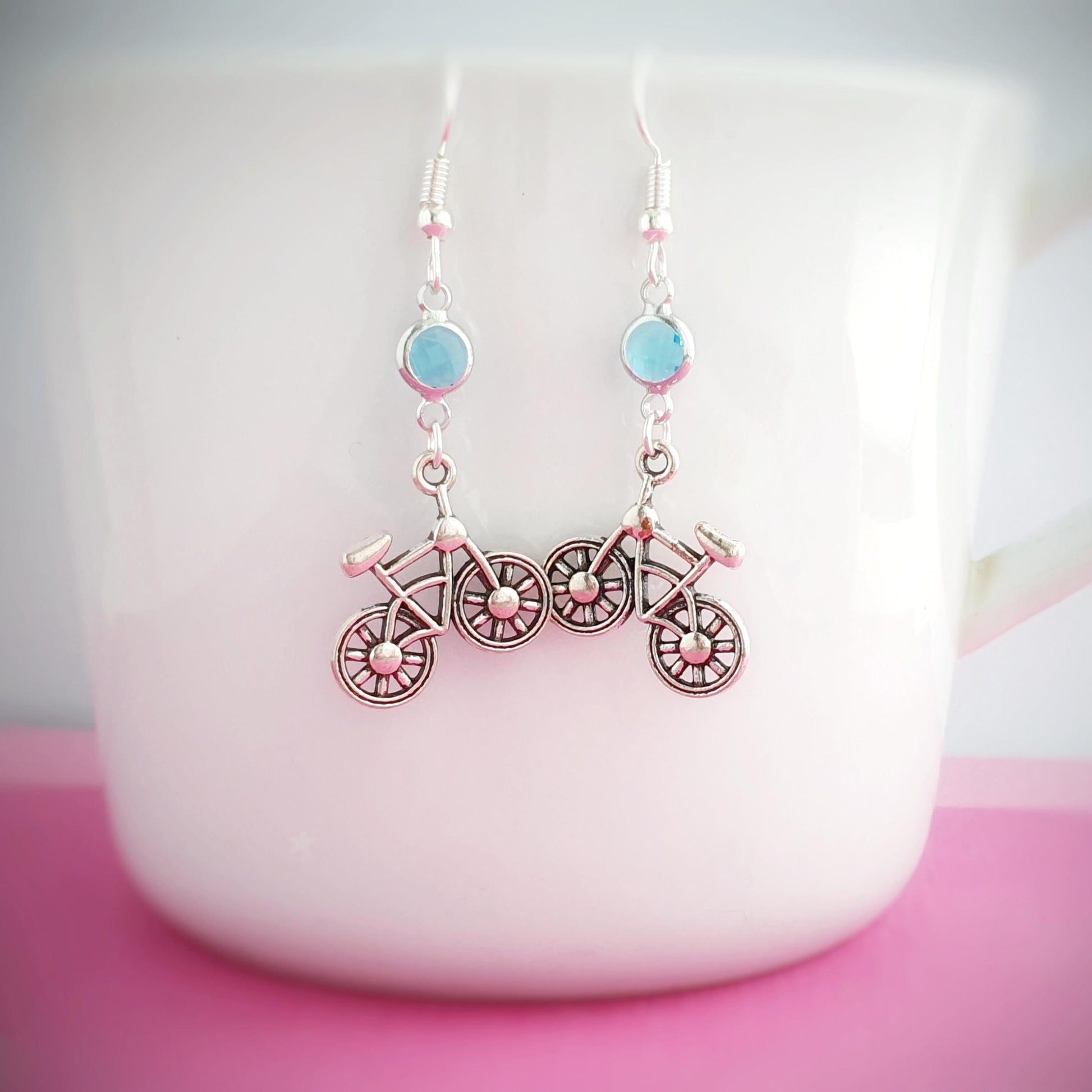 Bicycle-shaped earrings with blue birthstone charms on a white mug.