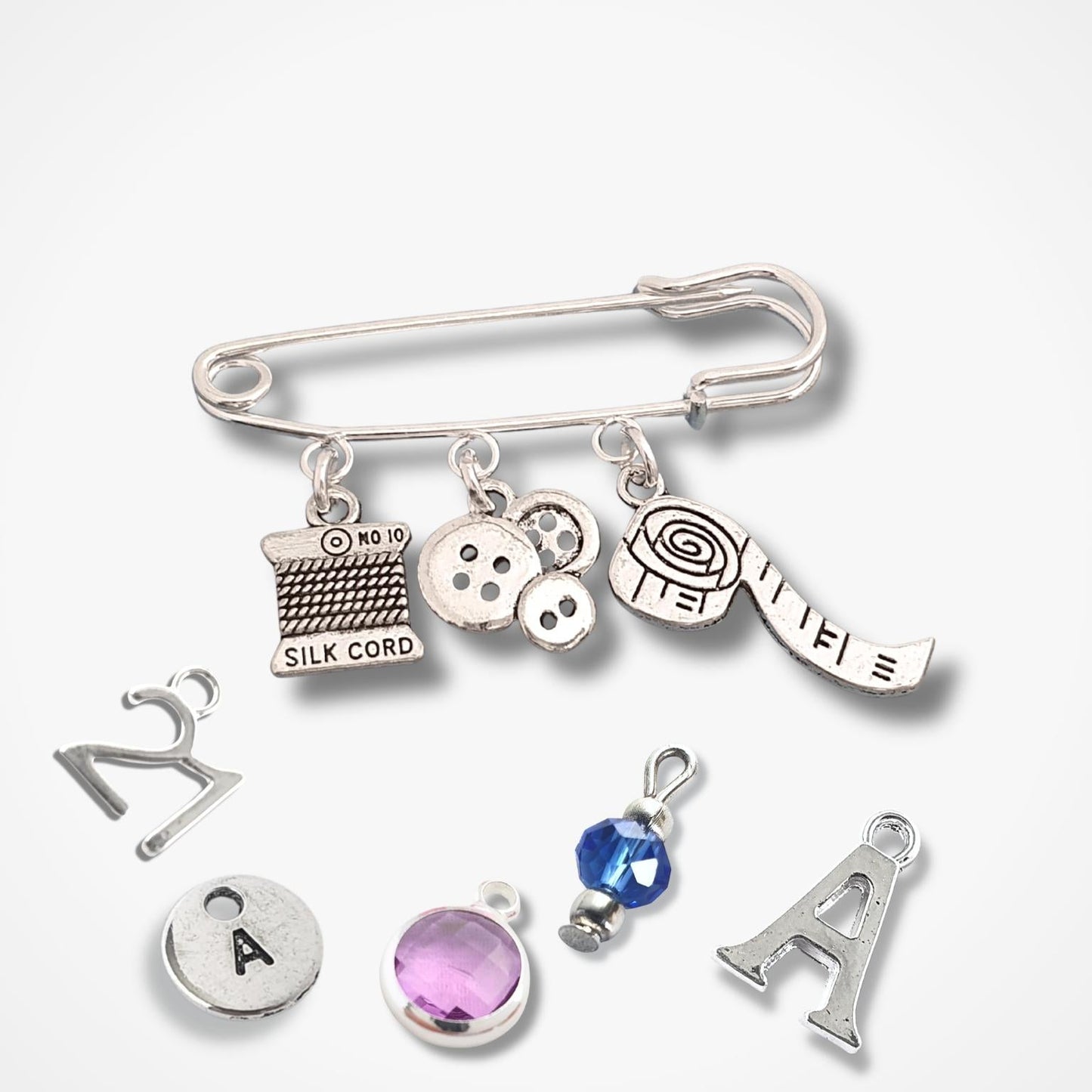 Silver charm brooch with various sewing theme charms on a white background