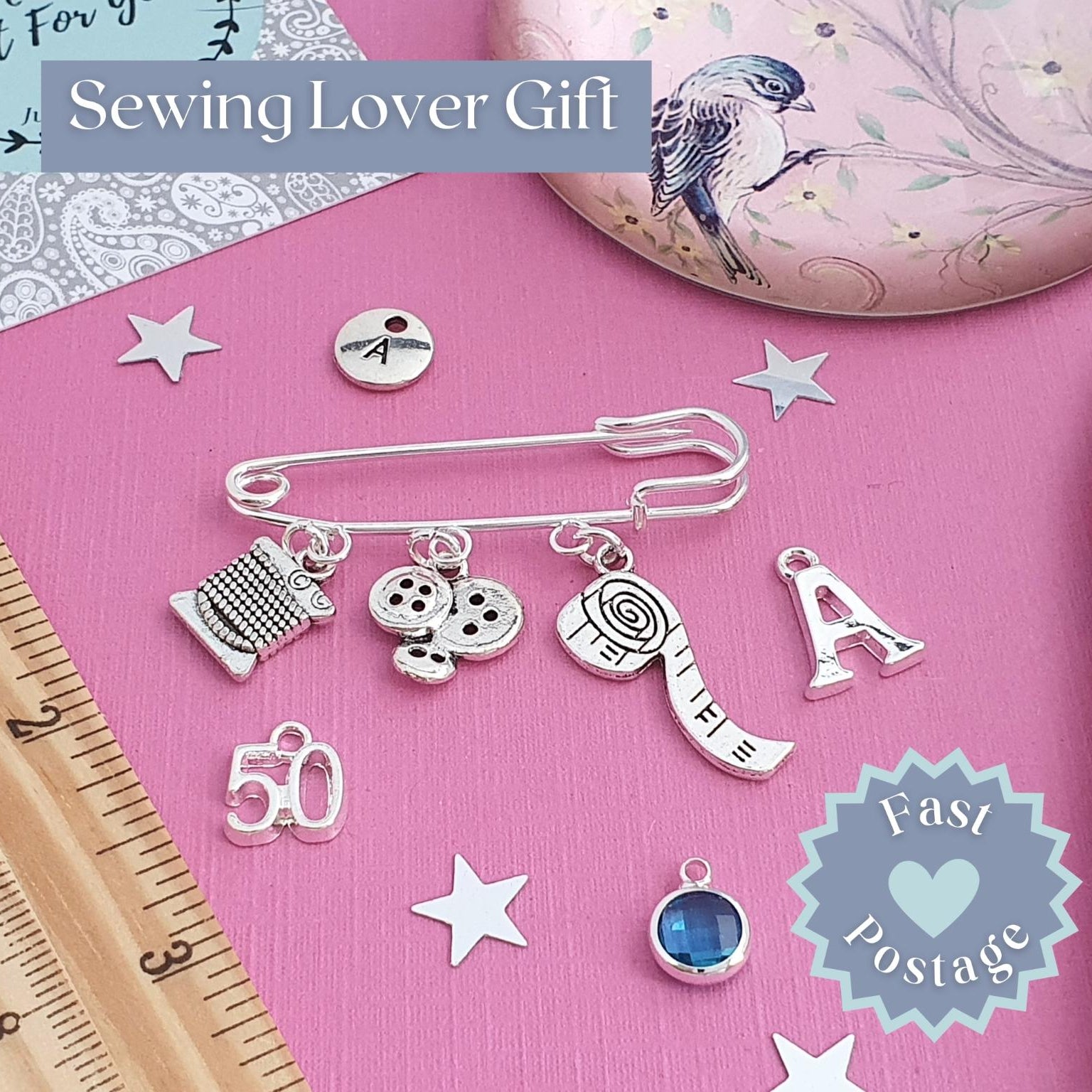 Sewing-themed brooch set with charms, pins, and a ruler on a pink background