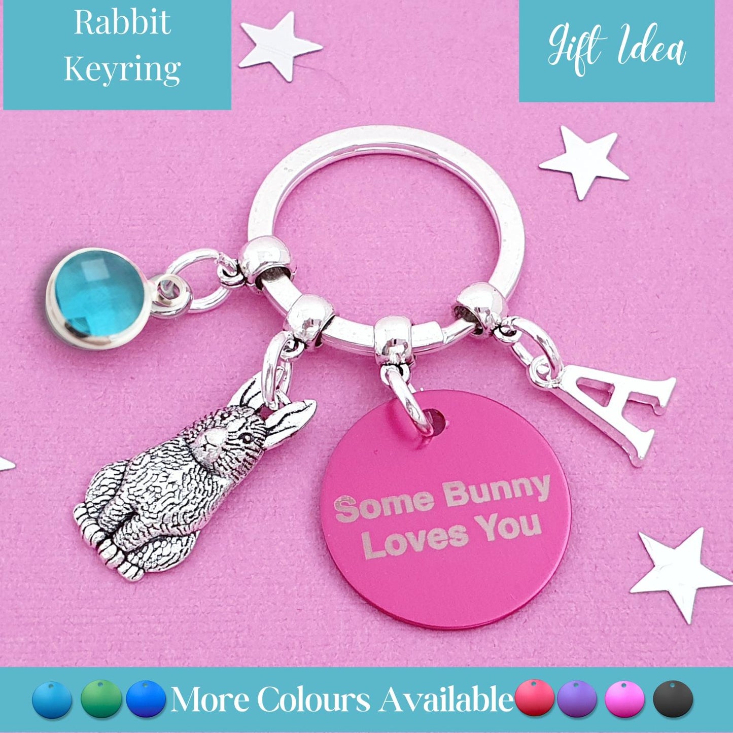 A silver-toned rabbit keyring charm set on a pink background, featuring a silver bunny charm, a round pink tag reading 'Some Bunny Loves You', a silver letter charm, and a blue oval stone charm. Text banners indicate 'Rabbit Keyring' and 'Gift Idea'.
