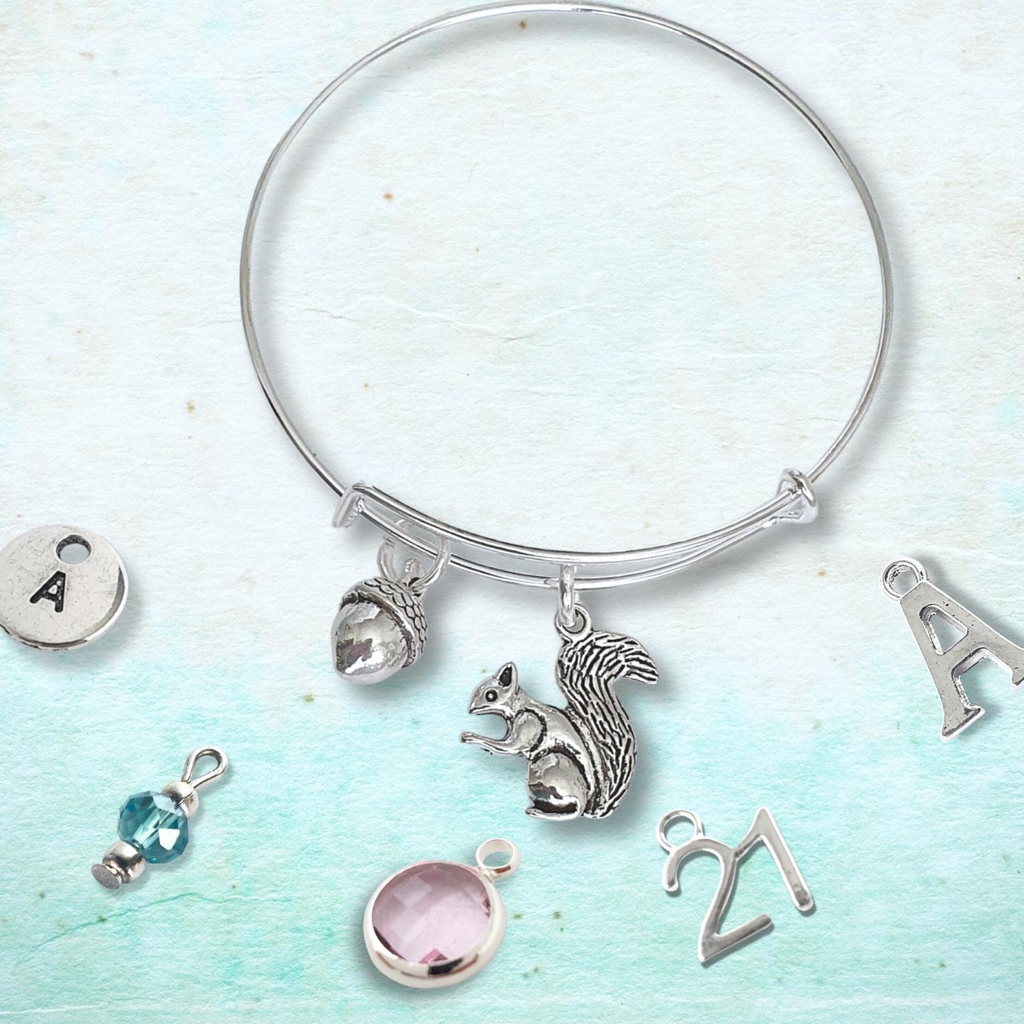 Silver adjustable squirrel and acorn bracelet with various charms on a light blue background