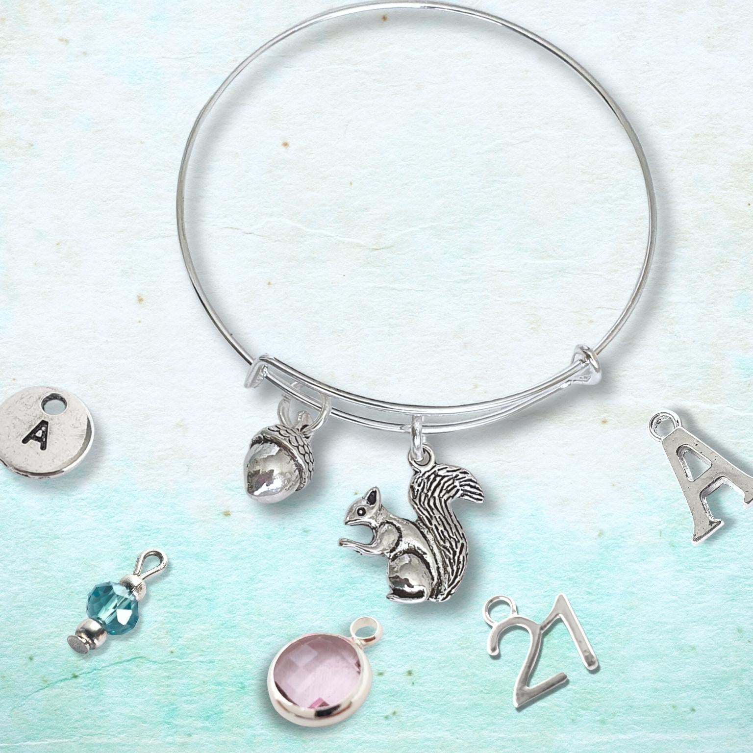Silver adjustable squirrel and acorn bracelet with various charms on a light blue background