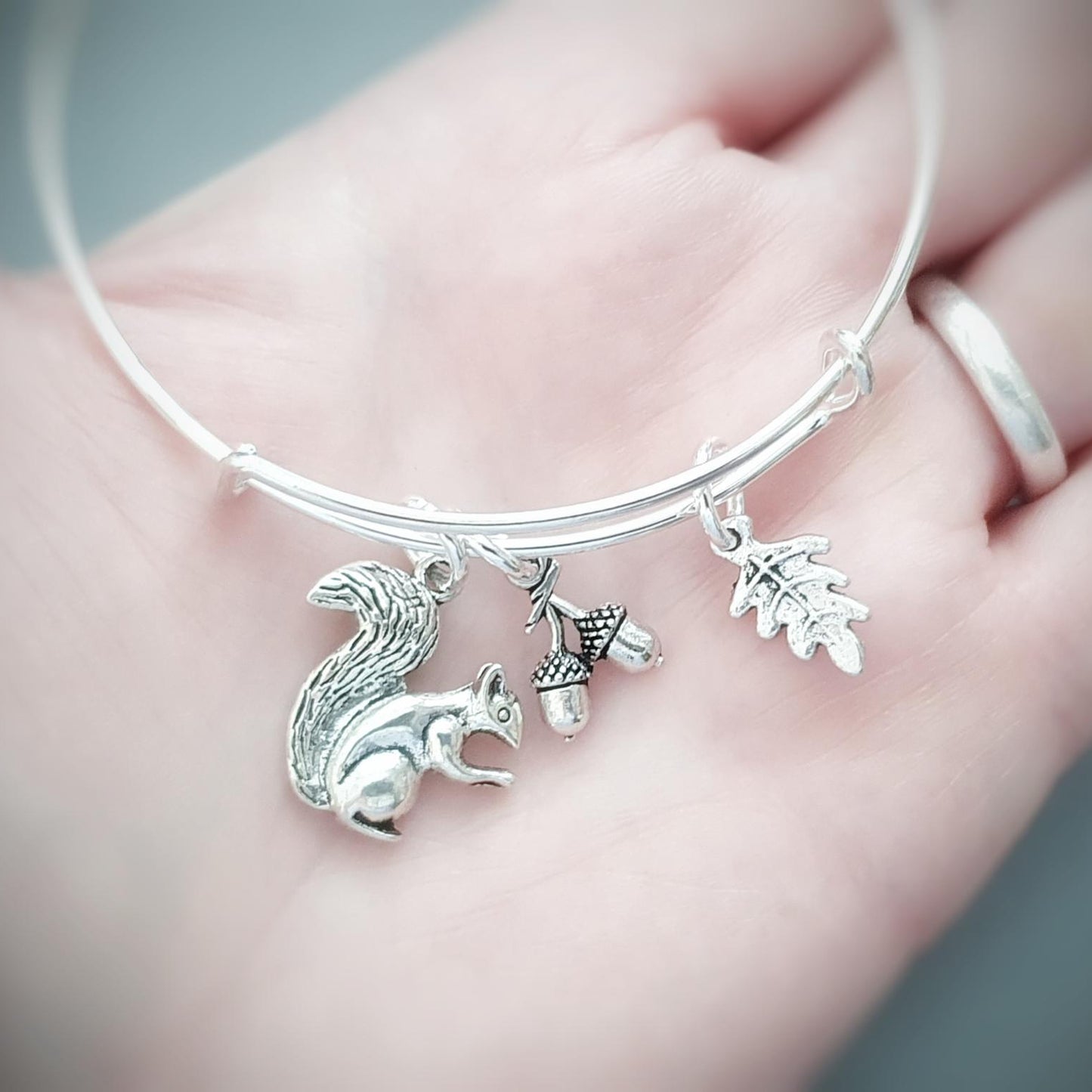 Silver bracelet with squirrel and acorn charms held in a hand.