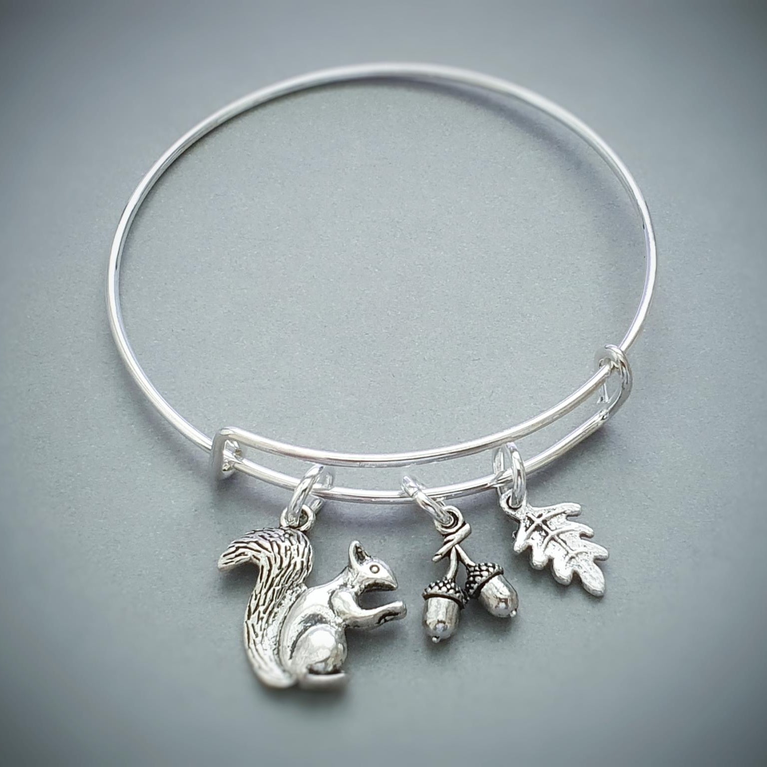 Silver bracelet with squirrel, acorn, and leaf charms on a gray background