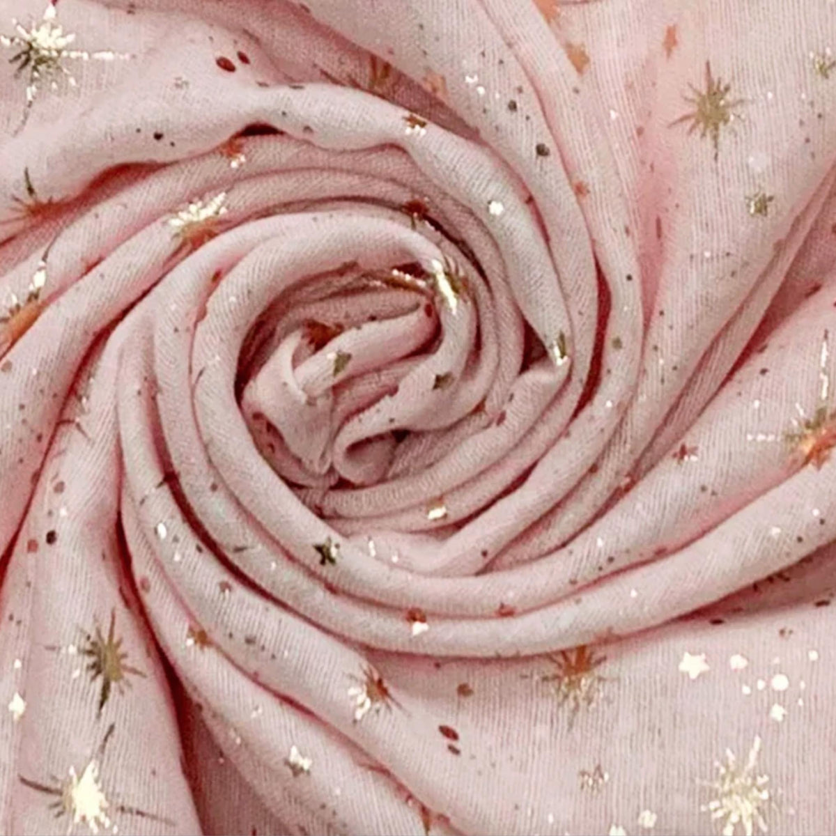 A close-up of a light pink sheer fabric arranged in a spiral, decorated with scattered metallic gold star and burst motifs.