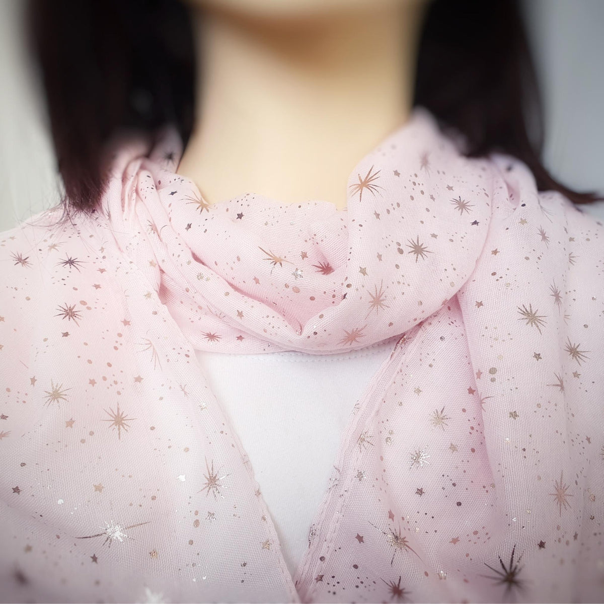 A close-up of a light pink sheer scarf with scattered metallic rose gold star and burst patterns, draped around a mannequin or model's neck.