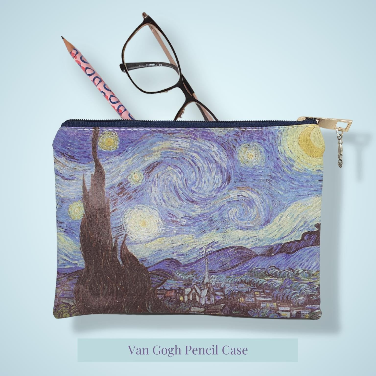 A zippered pencil case featuring a Van Gogh-inspired swirling night sky print in blue, yellow, and purple. A pink pencil and black eyeglasses are placed on top of the case, which is shown against a light blue background with a text label below reading 'Van Gogh Pencil Case'.