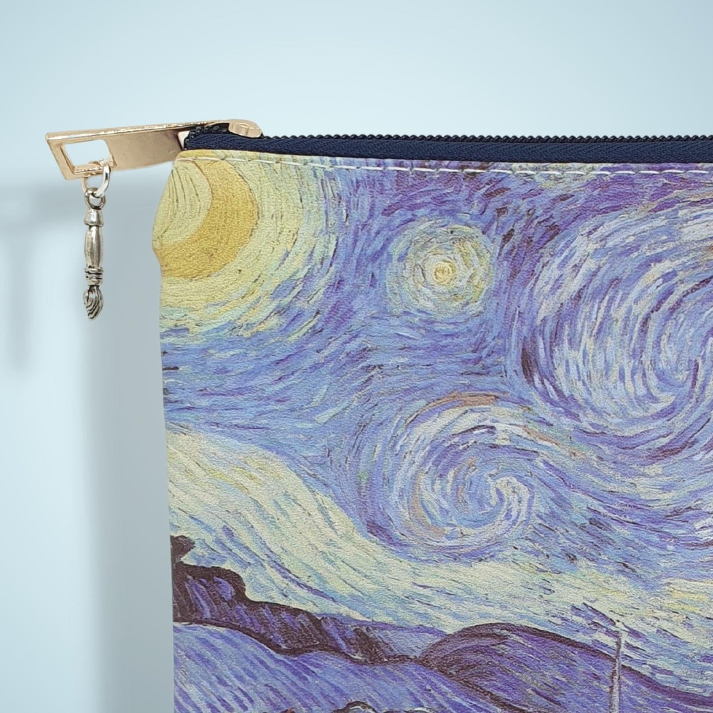 A close-up of a zipper pouch featuring a print of Van Gogh's Starry Night, with a gold zipper pull and a light blue background.