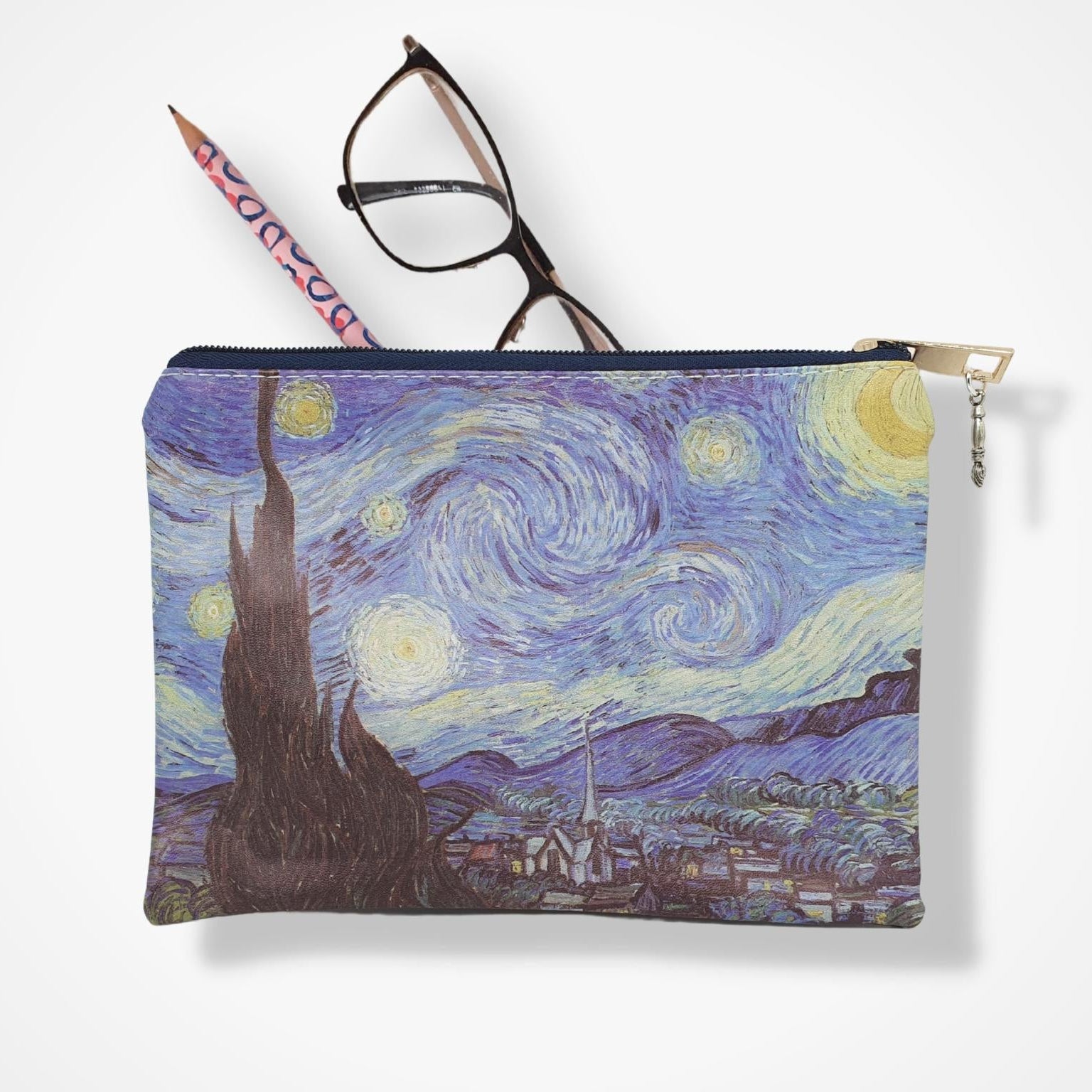 A zippered pouch featuring a print of Van Gogh's Starry Night, shown with a pencil and eyeglasses resting on top against a white background.