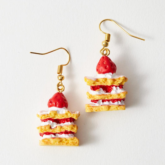 A pair of dangling earrings shaped like small strawberry shortcake slices, with gold fishhook wires, photographed on a plain white background.