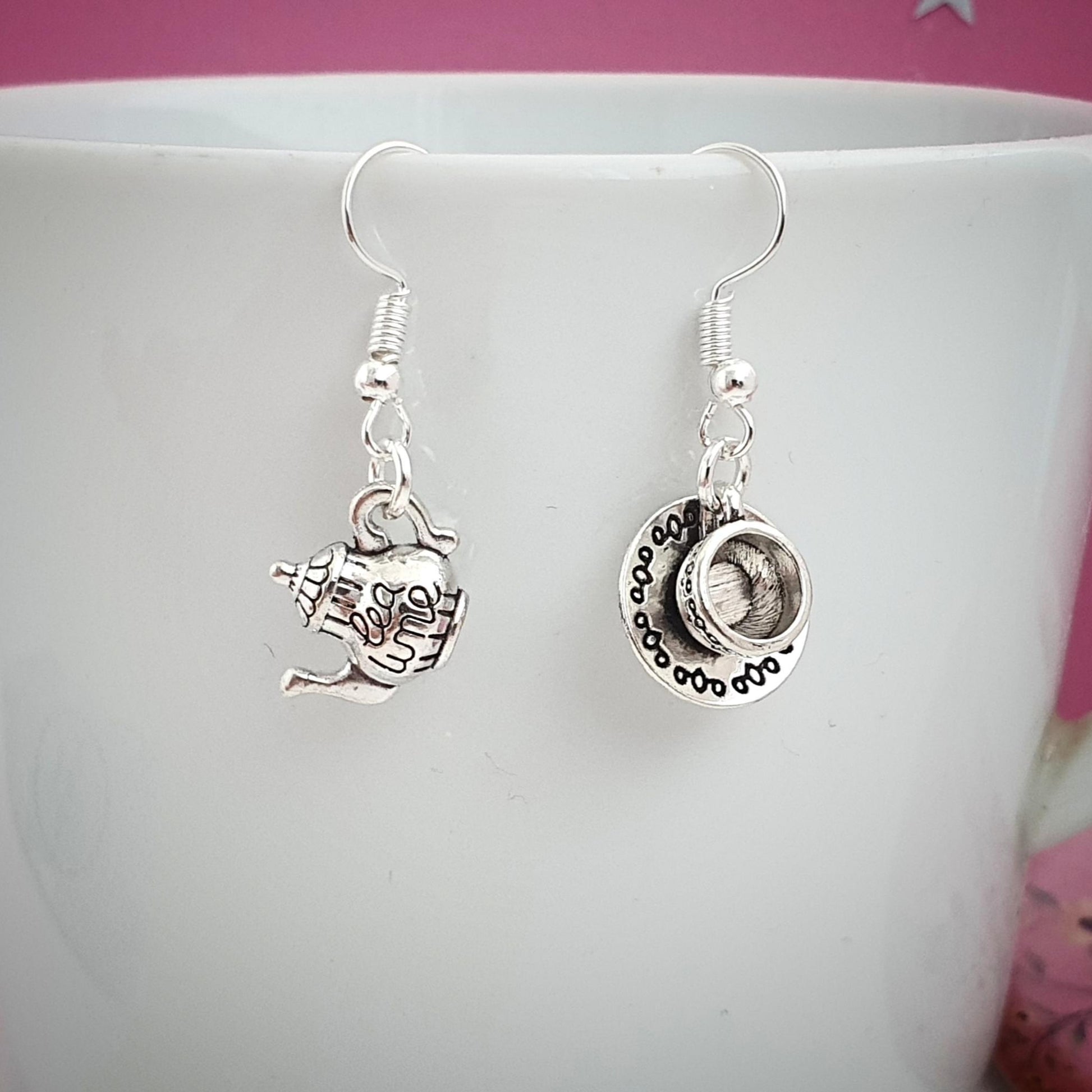 Silver earrings with charms on a white cup against a pink background