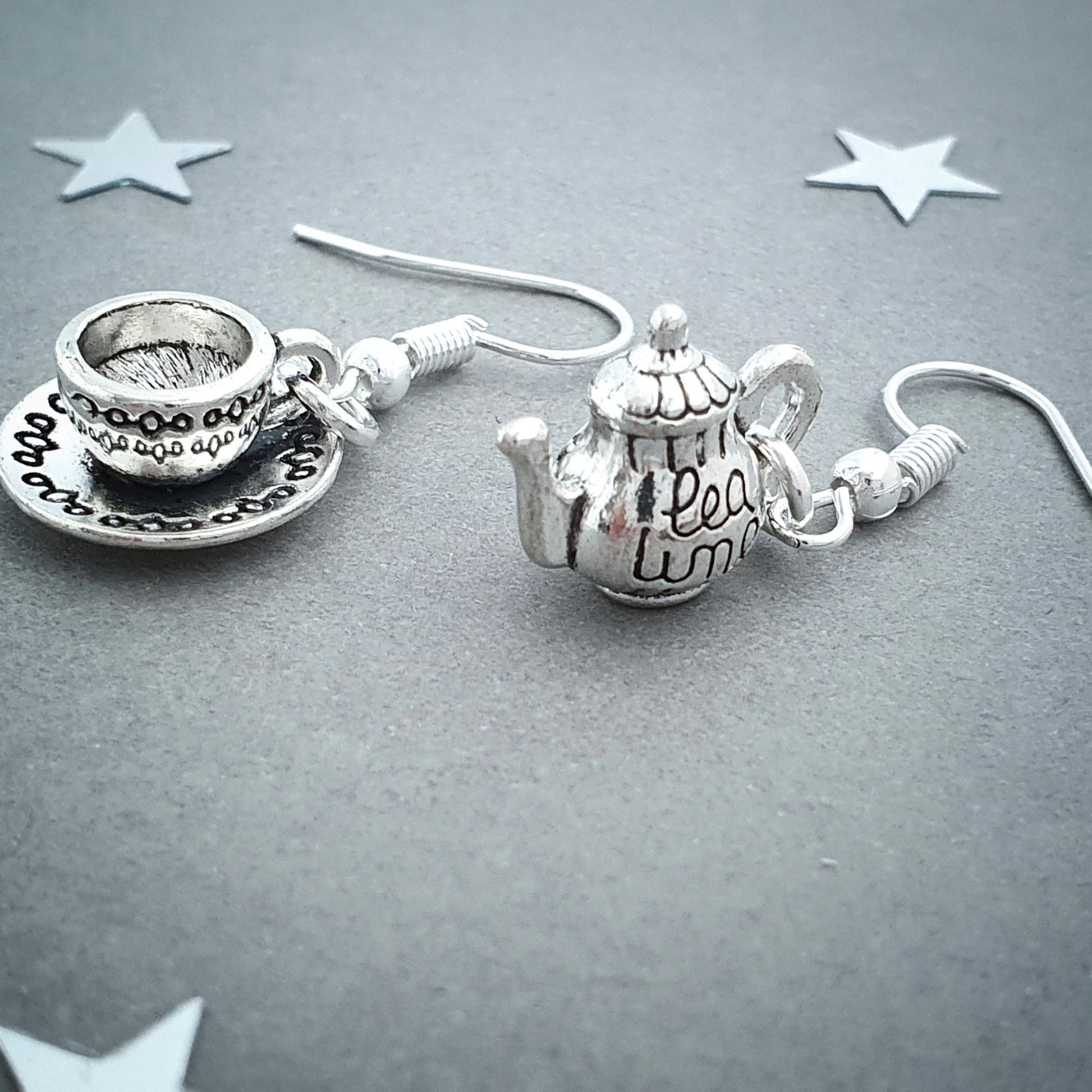 Silver teapot and teacup earrings on a gray background with star decorations.