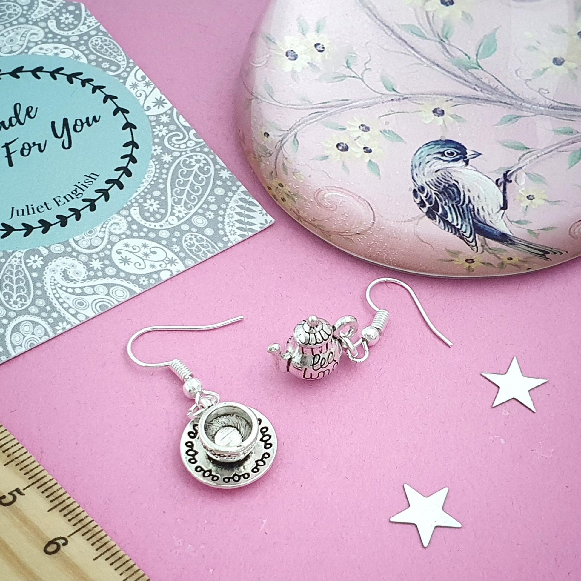 Silver earrings on a pink surface with a decorative stone and card in the background.