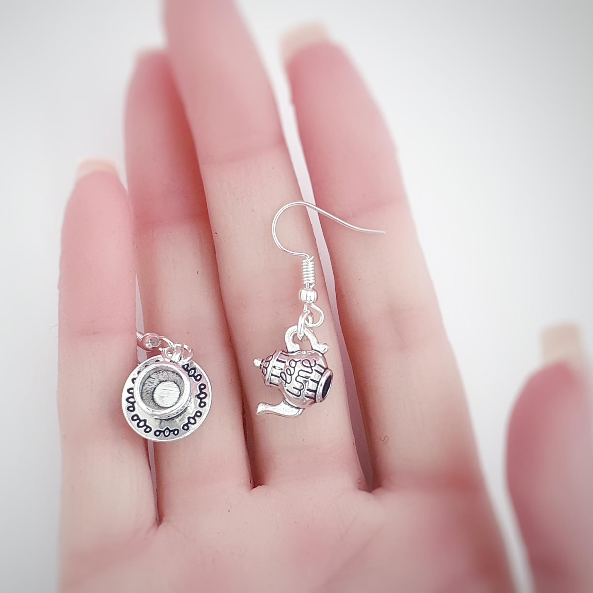 Silver earrings with charms held in a hand against a white background