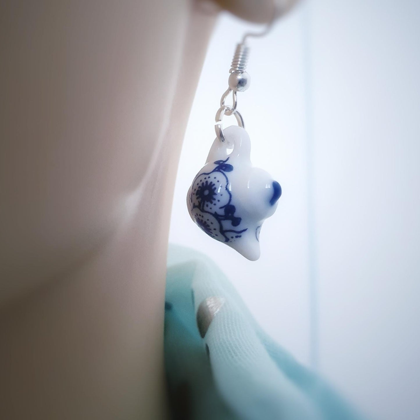 Earrings with blue and white teapot held against a blurred background