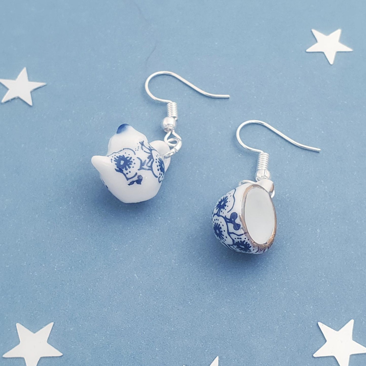 Pair of teapot and tea cup earrings with blue and white floral patterns on a blue background with star shapes.