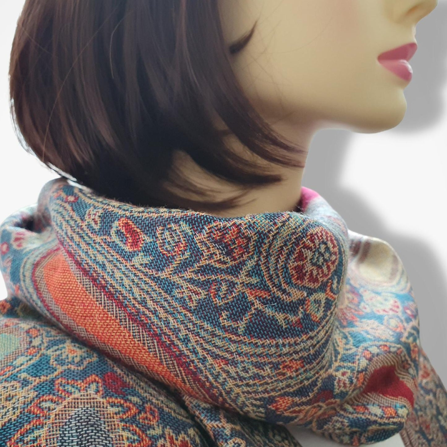 A close-up of a mannequin head with short dark brown hair wearing a patterned scarf in blue, rust orange, beige, and green tones against a plain light background.