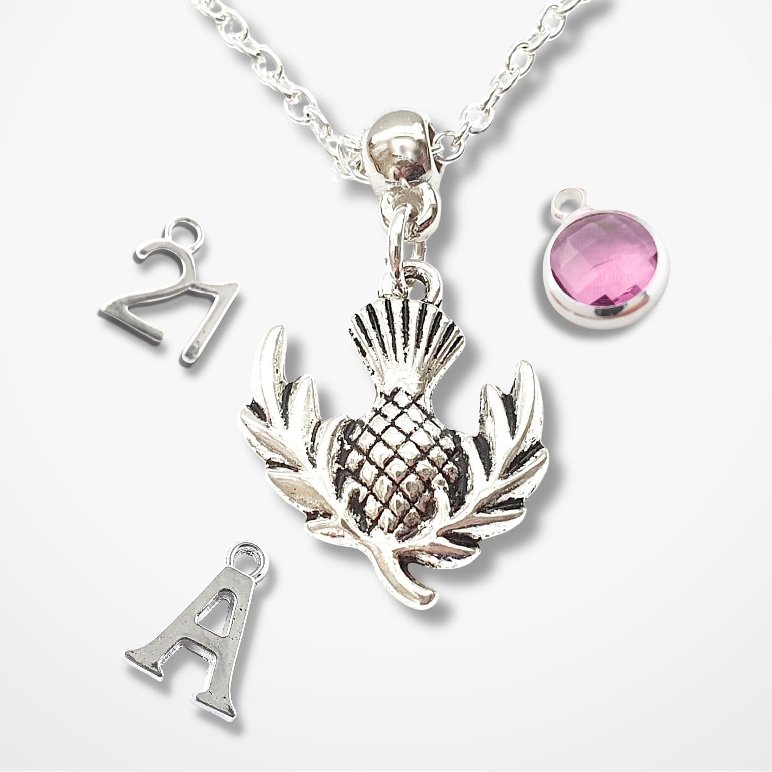 Silver necklace with thistle pendant, letter 'A' charm, and pink gemstone on a white background