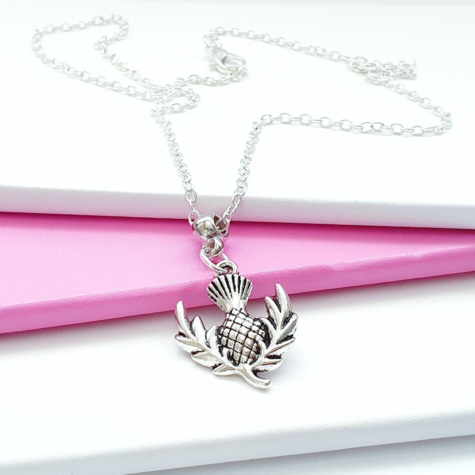 Silver necklace with a thistle pendant on a pink and white background