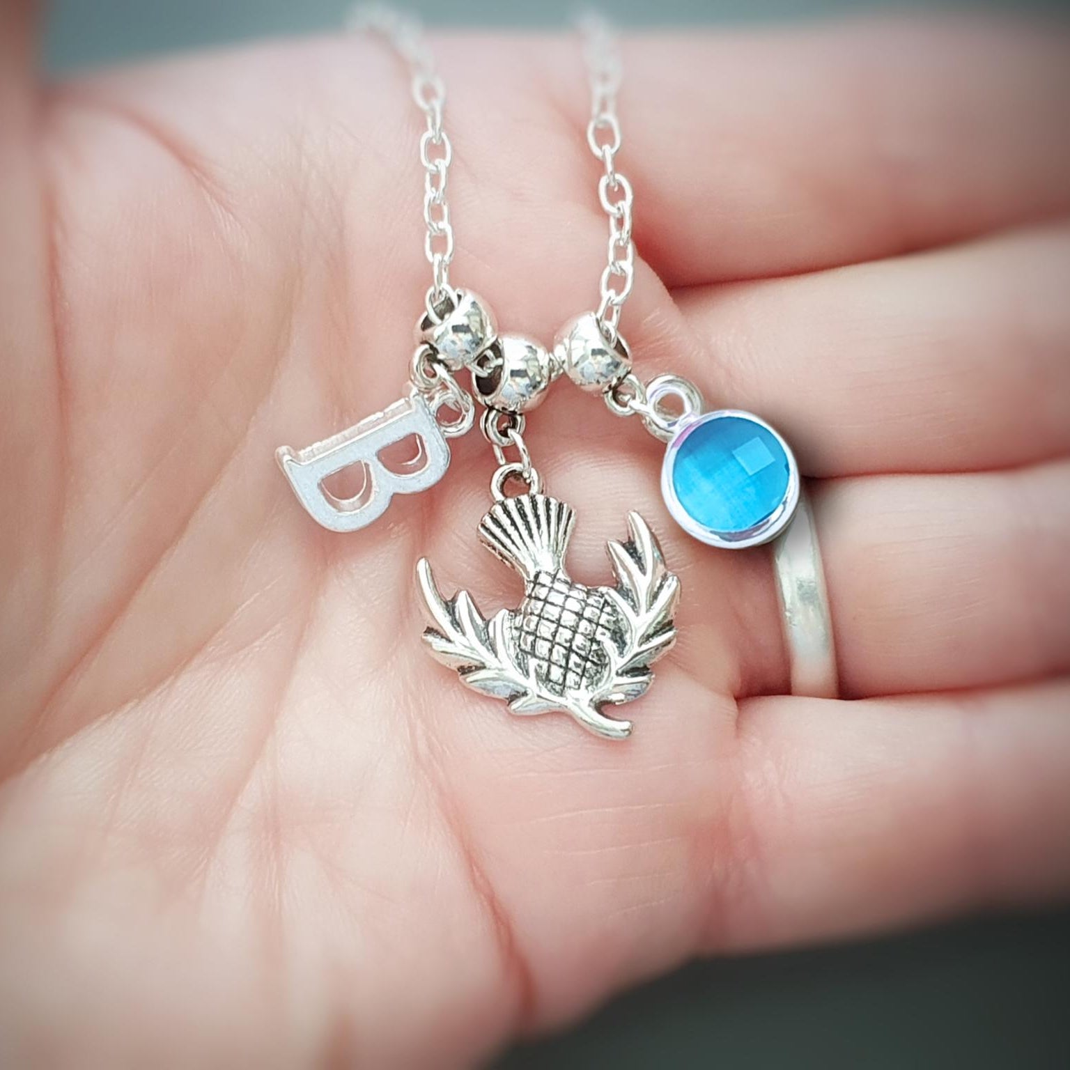 Close-up of a hand holding a silver necklace with various charms.