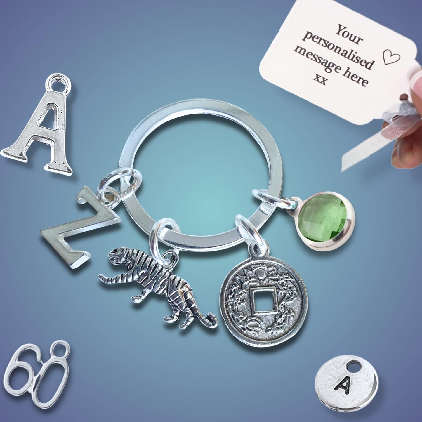 Silver keychain with tiger charm and coin charm and a hand holding a card for personalization on a gradient blue background.