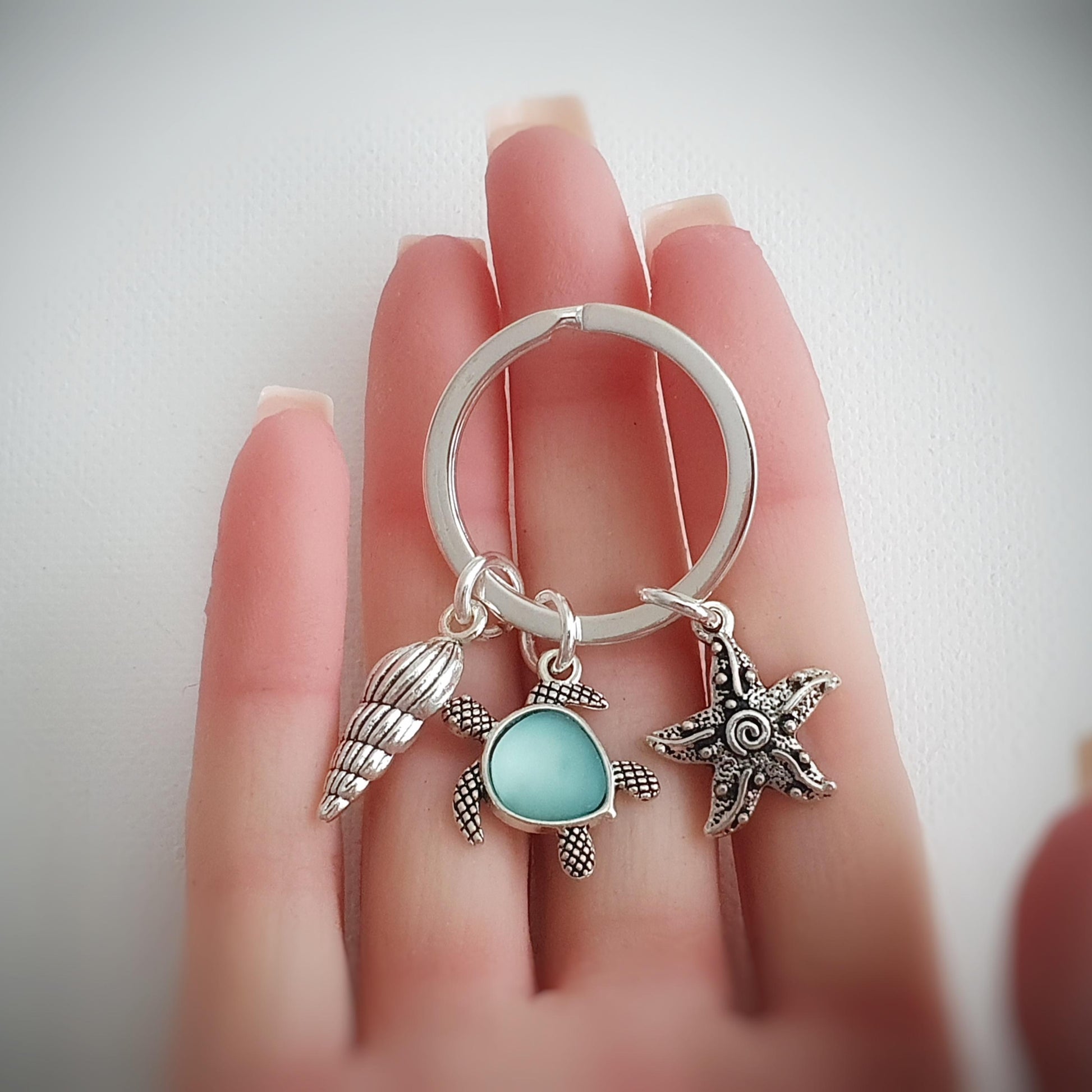 Silver keychain with turtle and starfish charms held by a hand on a light background