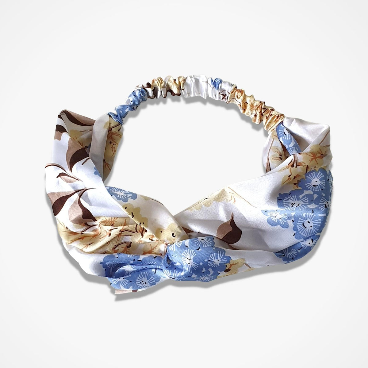 A silk-like headband with a knotted bow design, featuring a blue and brown floral pattern on a white background, displayed on a clean white studio background.