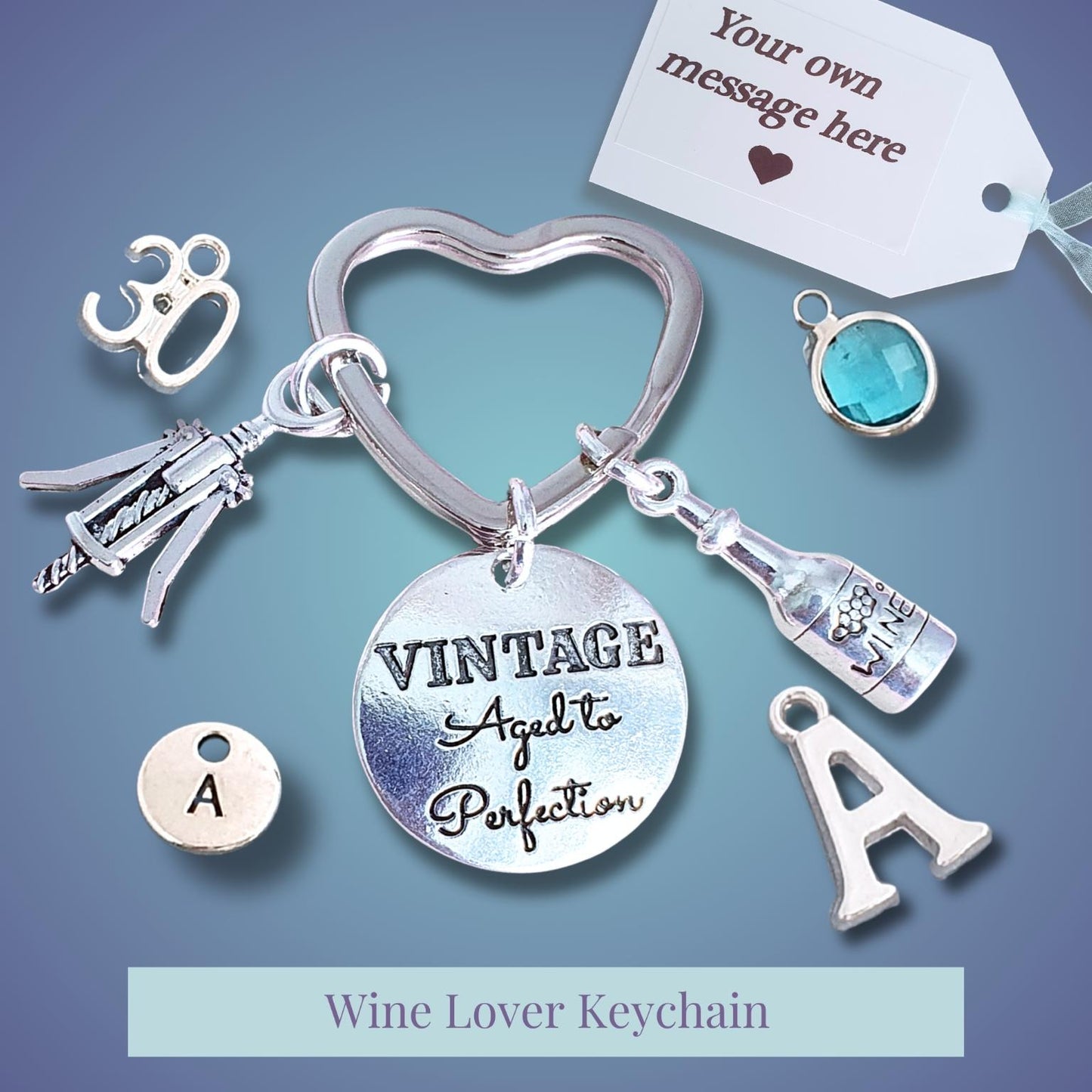 A silver-tone wine-themed keychain charm set on a blue gradient background, featuring a heart-shaped ring, a round disc engraved 'VINTAGE Aged to Perfection,' bottle and corkscrew charms, an 'A' letter charm, a small turquoise stone charm, and a customizable message tag.