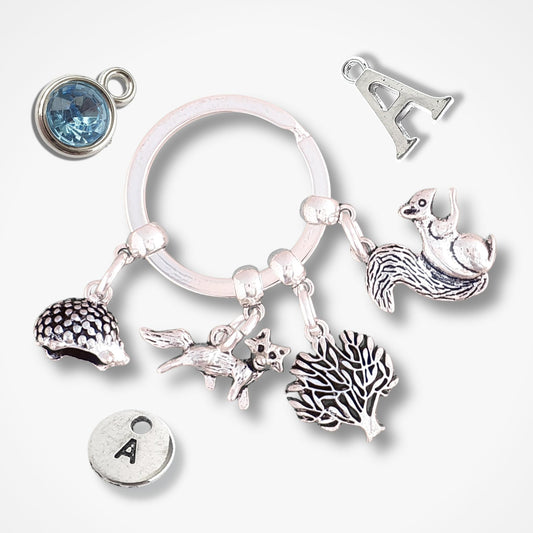 Silver keychain with hedgehog, fox, tree and squirrel charms on a white background