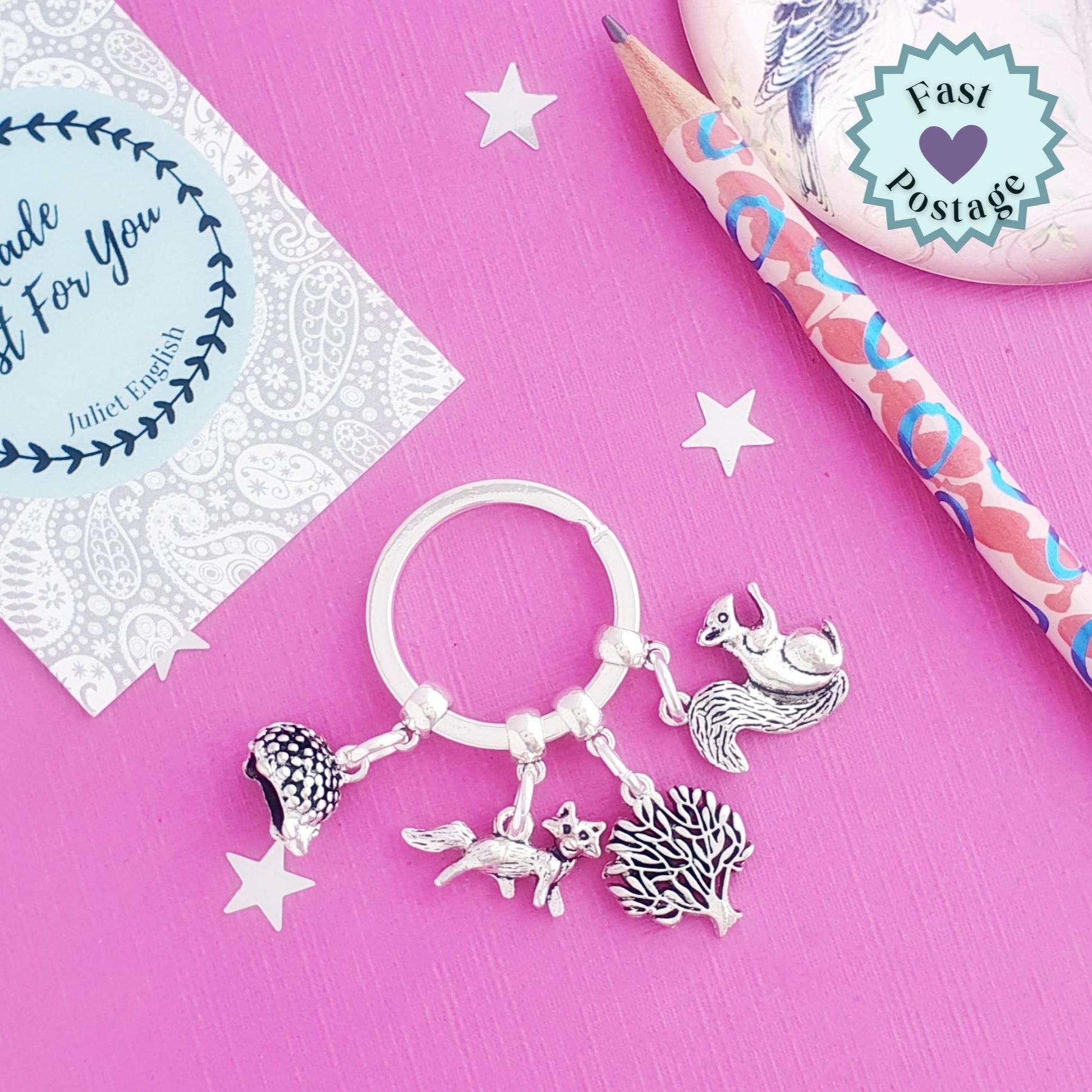 Silver wodland animal charm keyring on a pink background with a card and pencil.
