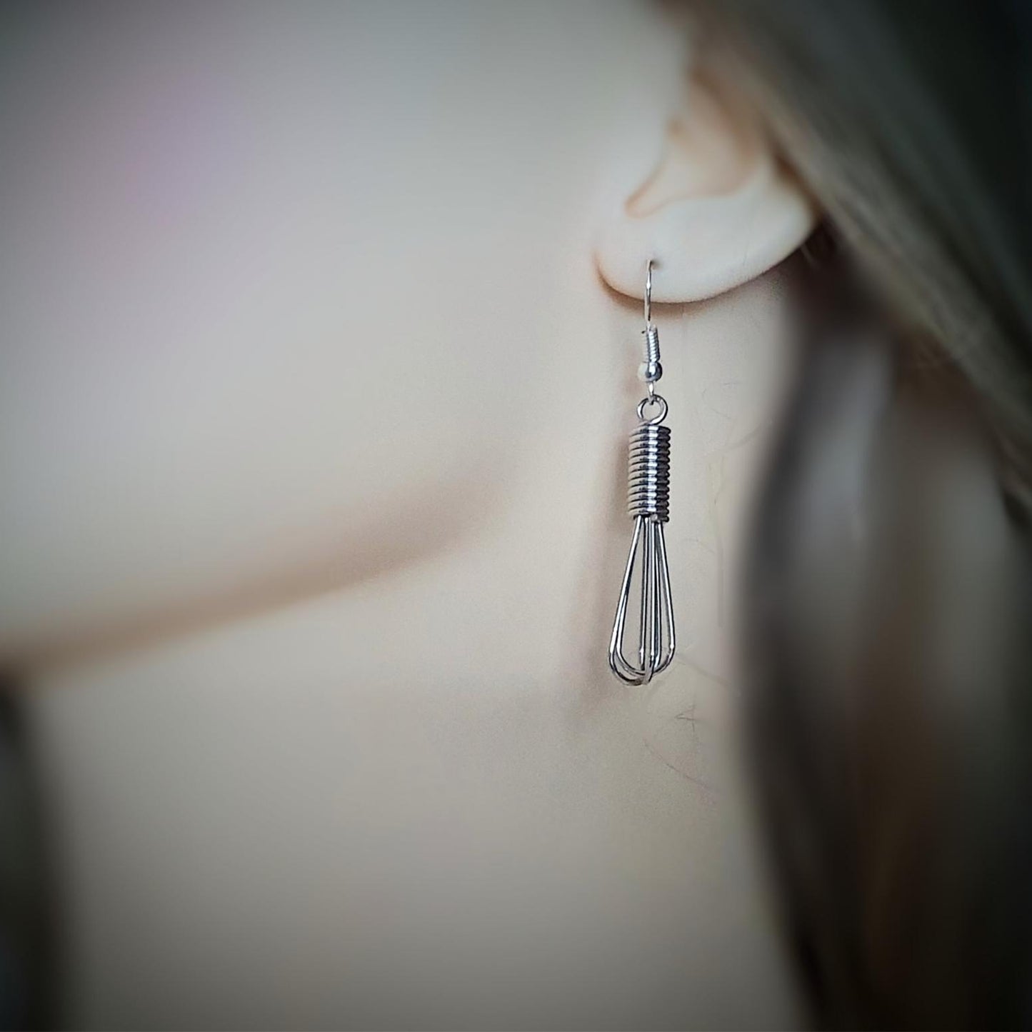 Close-up of a person wearing a unique earring with a whisk design.
