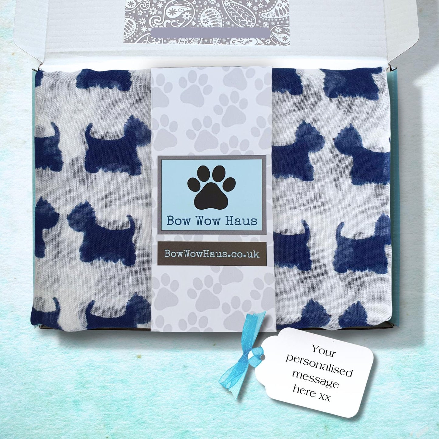 A custom white scarf printed with dark blue dog silhouettes, folded inside a white gift box. The center of the blanket has a light blue band with a black paw print and the text 'Bow Wow Haus' and 'BowWowHaus.
