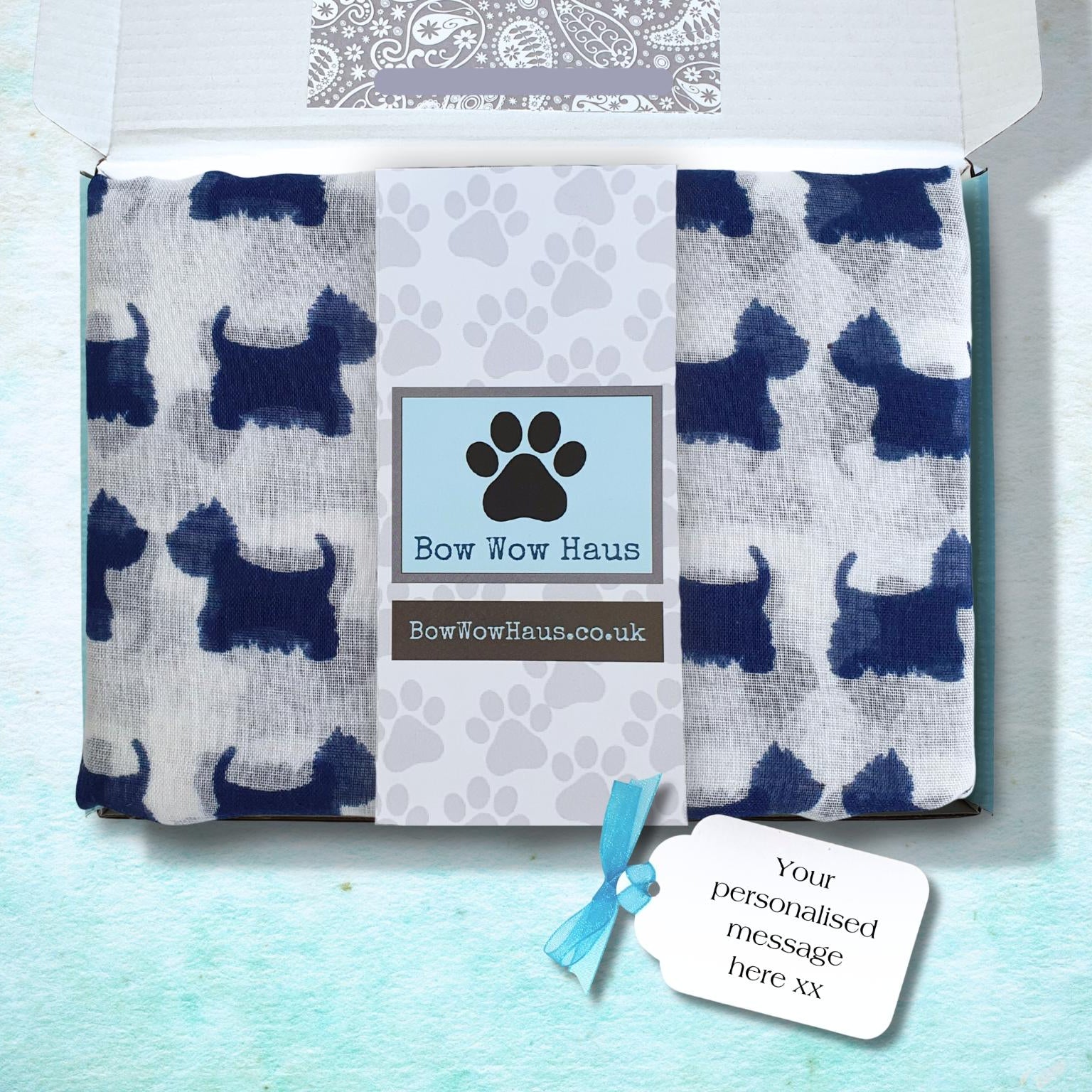 A custom white scarf printed with dark blue dog silhouettes, folded inside a white gift box. The center of the blanket has a light blue band with a black paw print and the text 'Bow Wow Haus' and 'BowWowHaus.