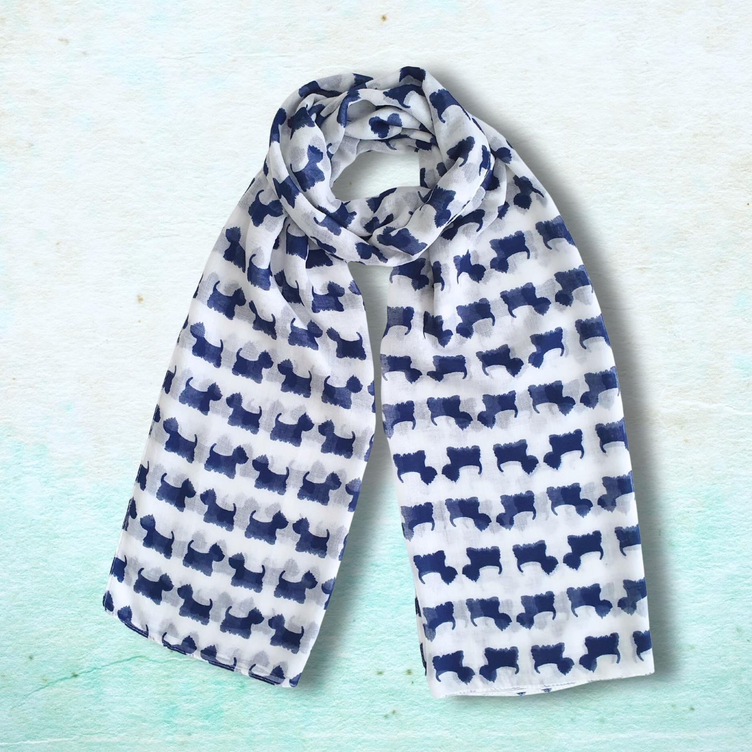 A lightweight white scarf with a repeating navy blue dog silhouette pattern, styled in a loop on a textured light blue background.