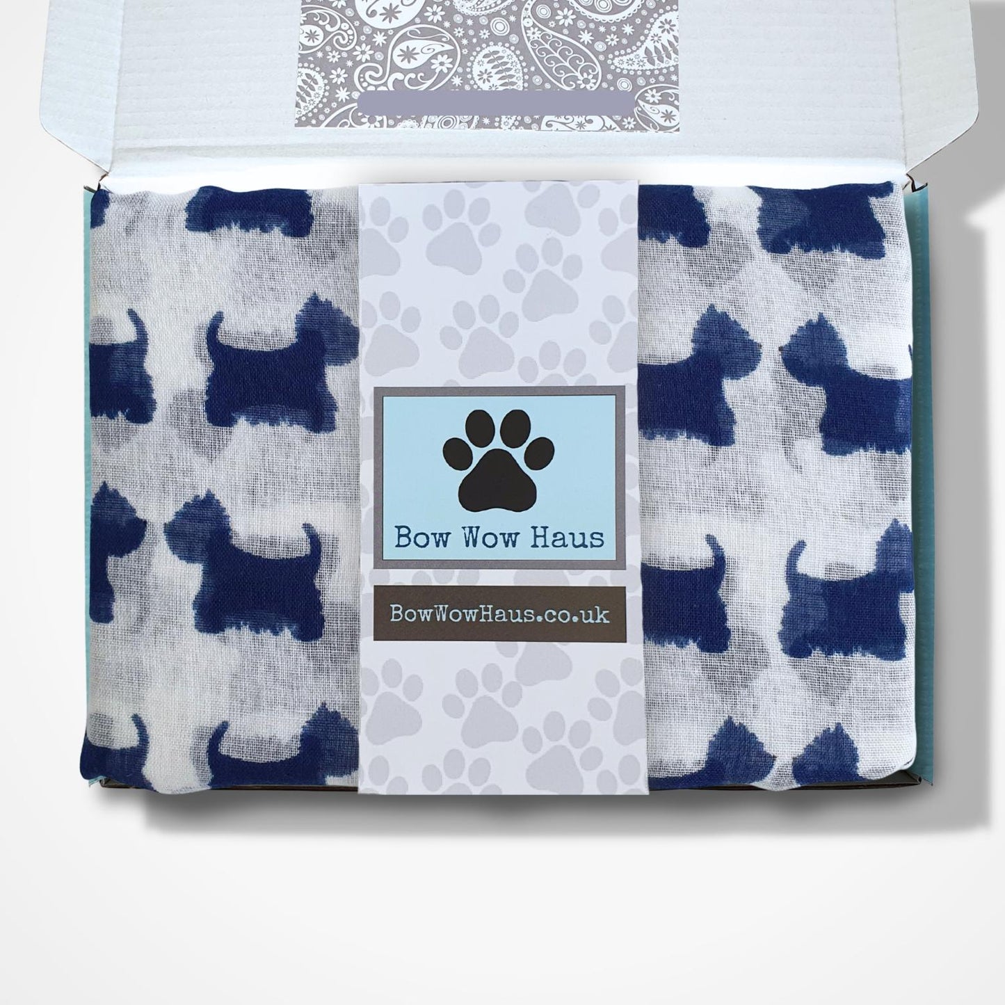 A packaged gift box from Bow Wow Haus, shown open from above on a white background. The contents are a folded white scarf printed with dark blue dog silhouettes and a central white band with a blue paw-print label reading Bow Wow Haus.