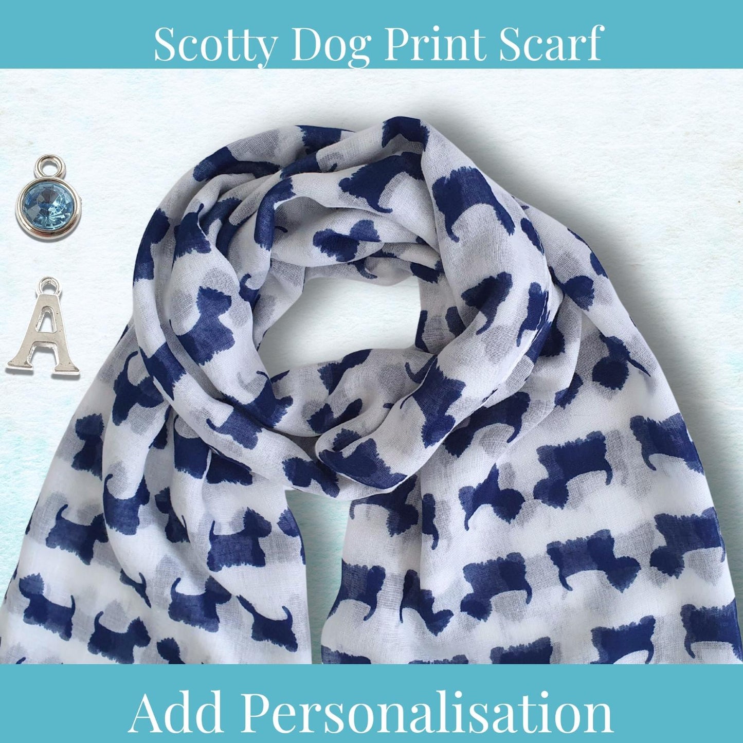 A white scarf with a navy blue Scotty Dog print pattern, styled with two silver charms (a blue gemstone pendant and a letter 'A') on a light blue textured background. Text overlays read 'Scotty Dog Print Scarf' at the top and 'Add Personalisation' at the bottom.