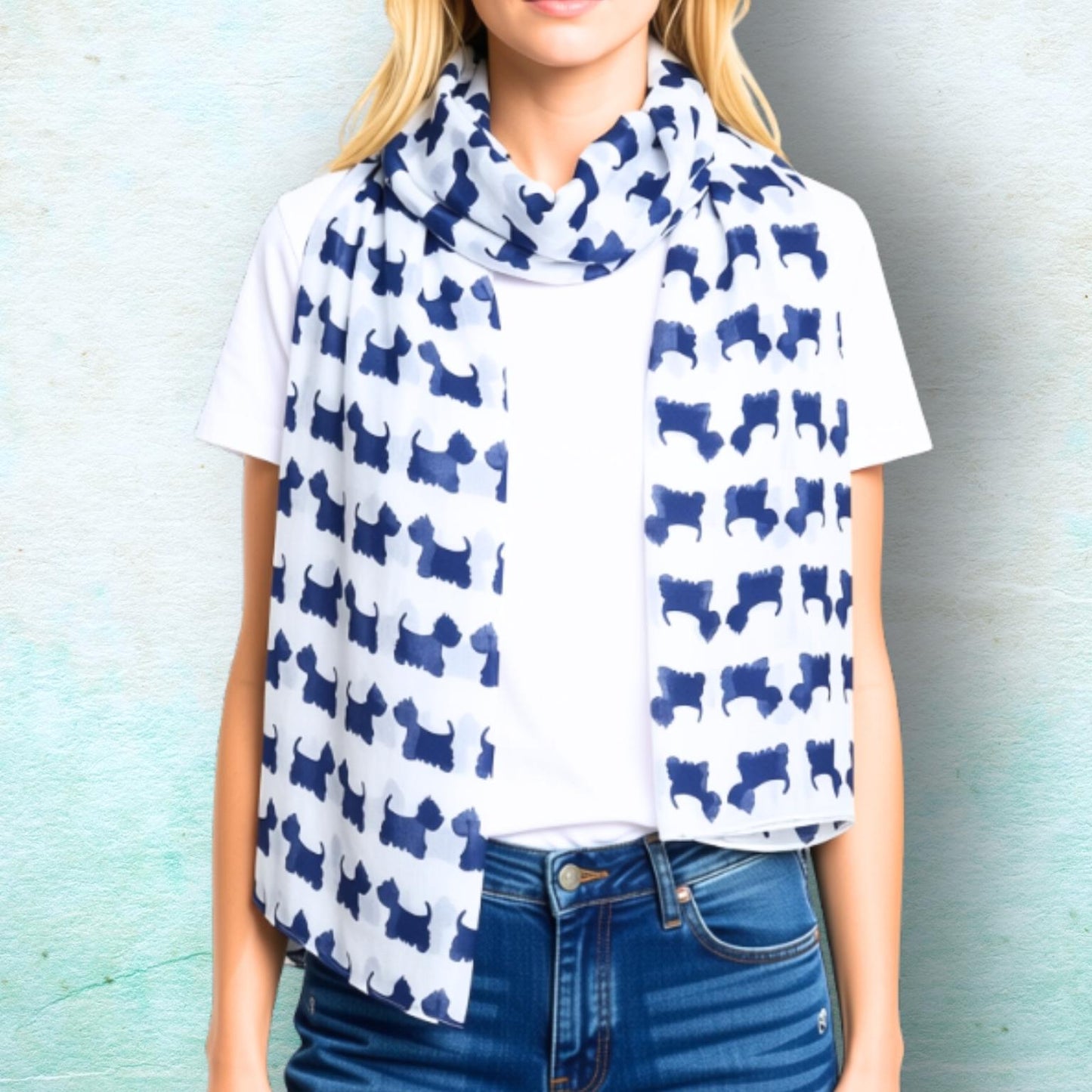 A woman wearing a white scarf with a repeating navy blue dog silhouette pattern, styled over a white t-shirt and blue jeans against a textured light blue wall.